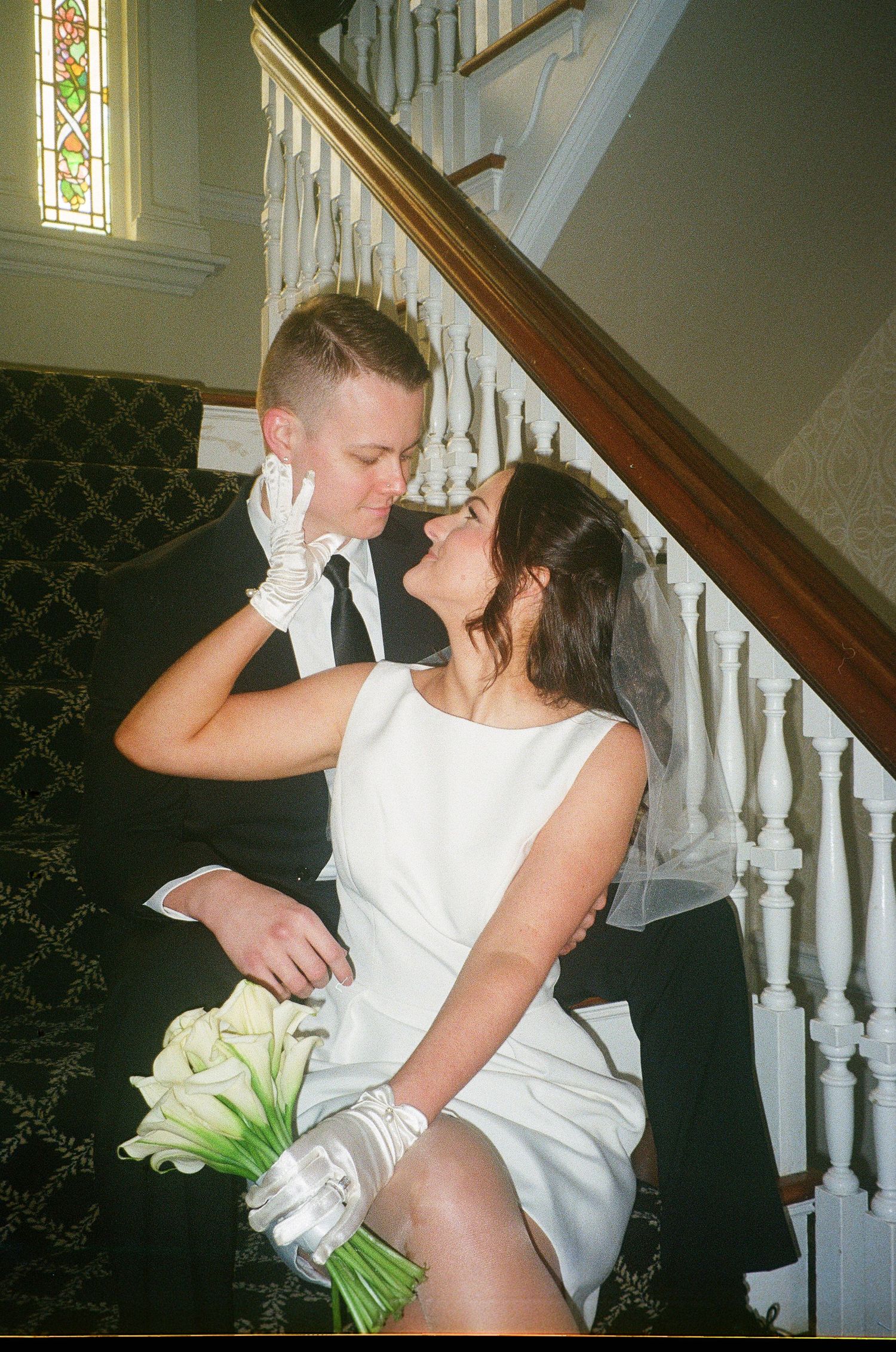 Wedding couple embracing on elegant staircase with white banister.
