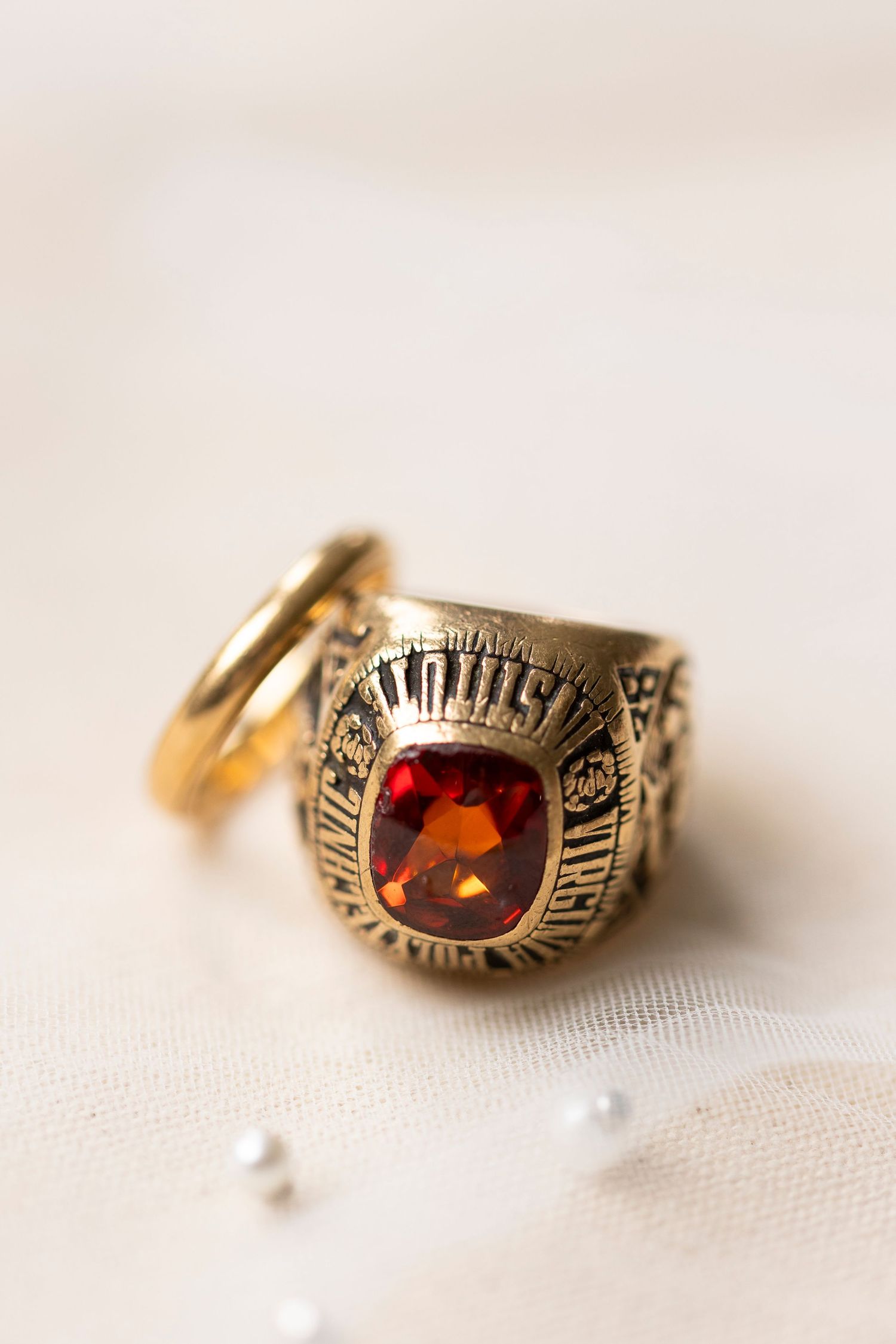 Vintage gold class ring with red gemstone photographed on white textile.