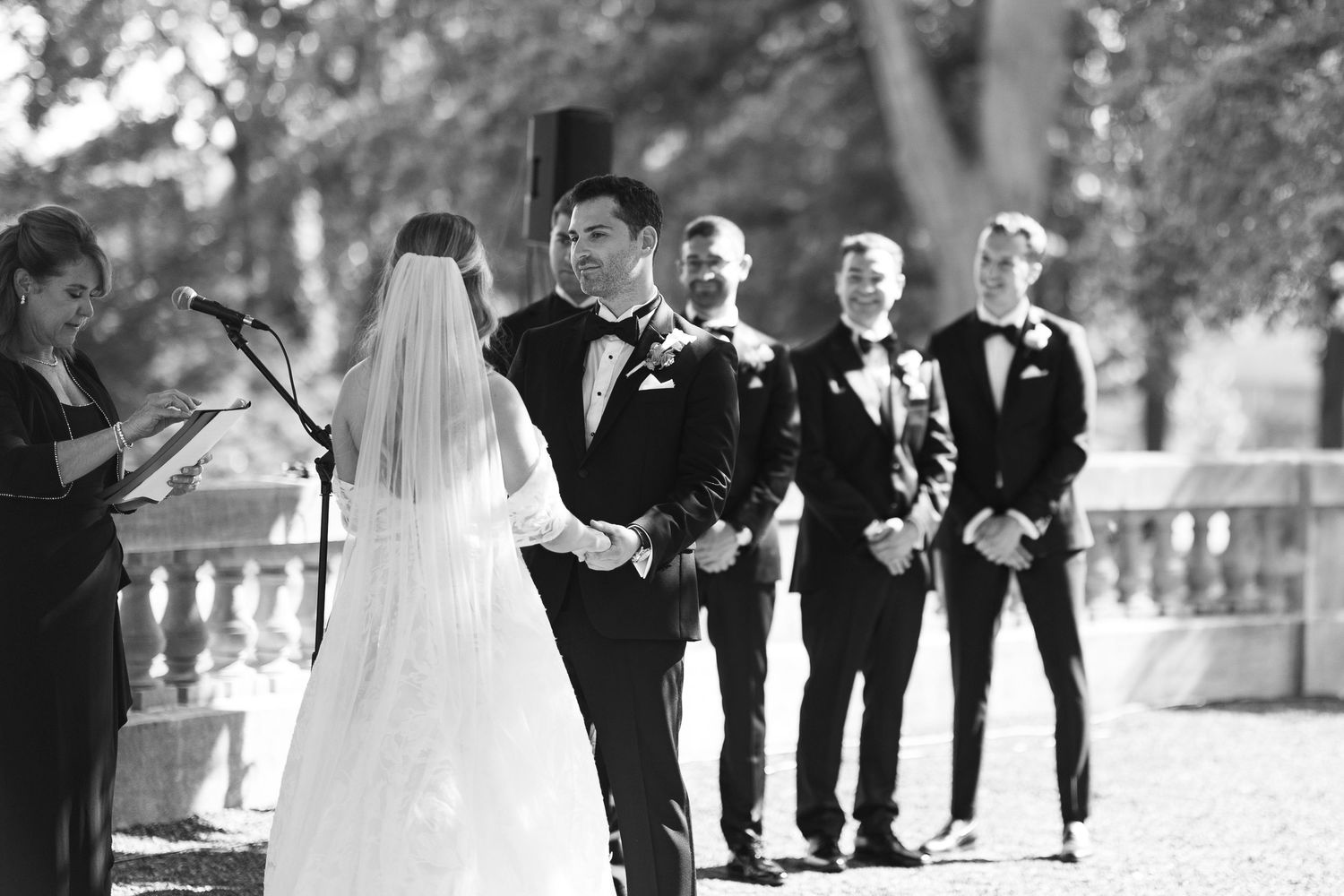 Wedding party members walk along a path during an outdoor ceremony.