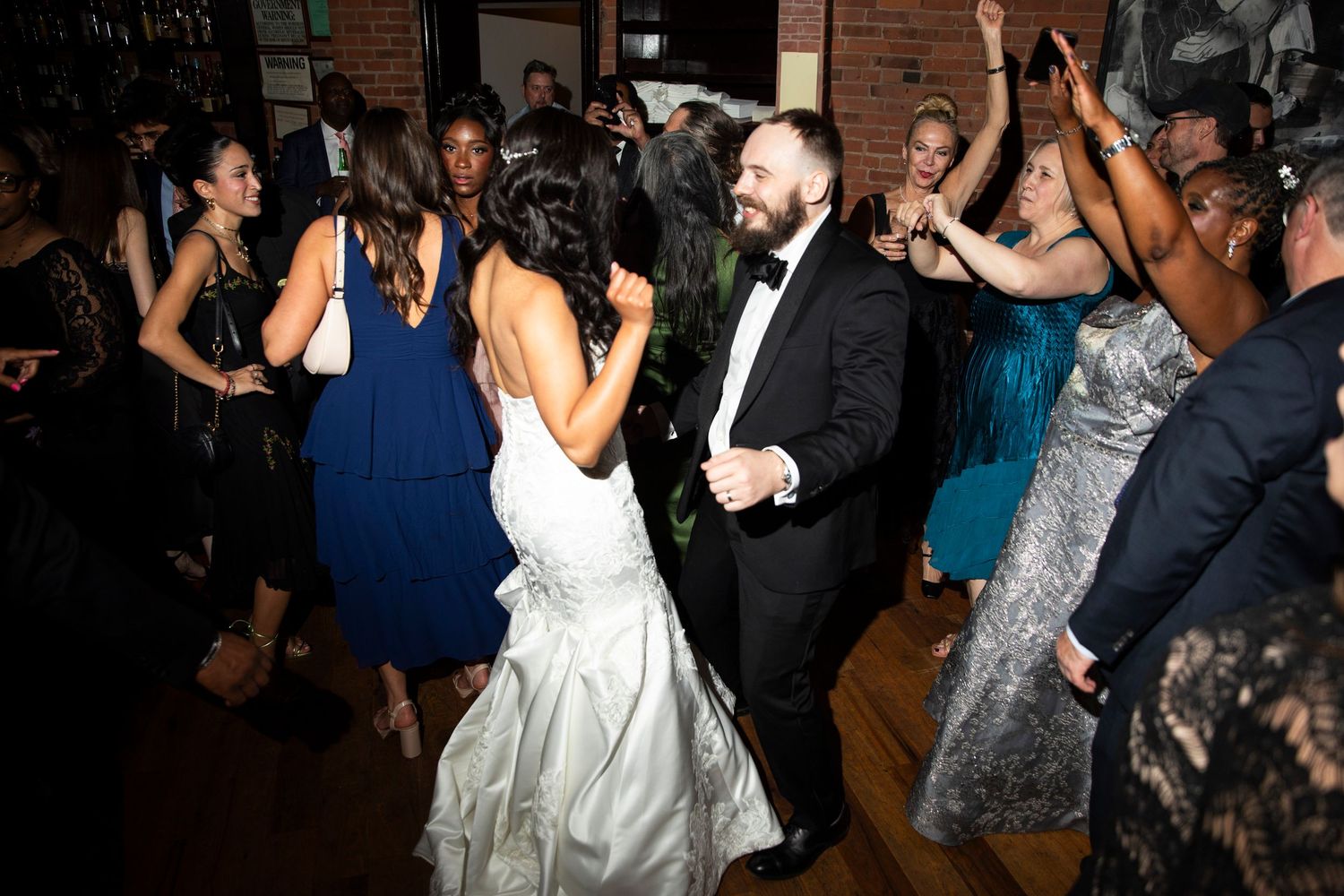 Wedding reception guests dancing and celebrating on a crowded dance floor with festive lighting.