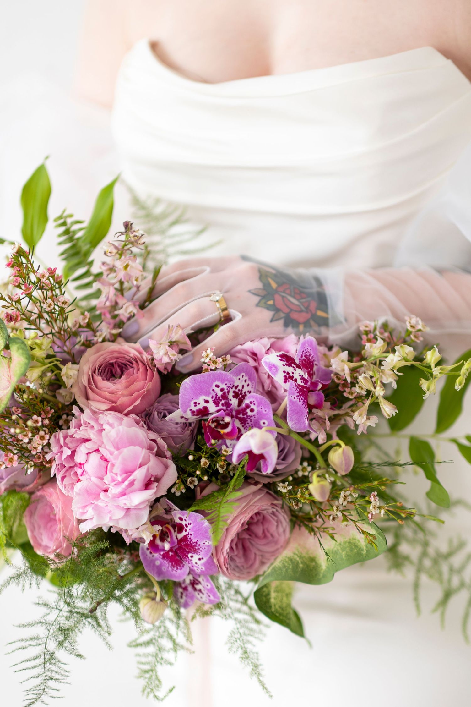 Pink and purple flowers with ferns arranged in an elegant display on white.