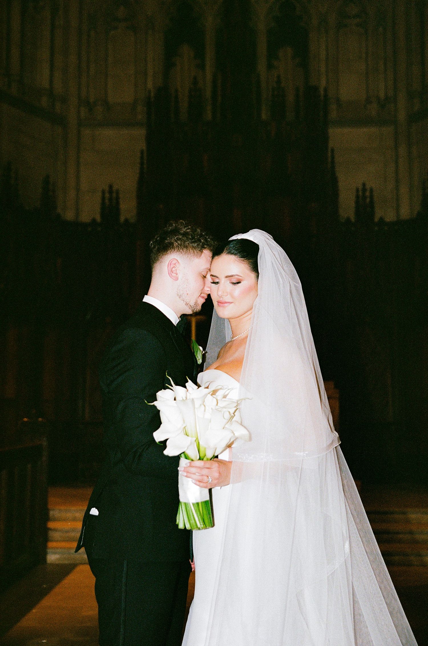 Intimate wedding ceremony moment in a dramatic cathedral setting with white lilies.