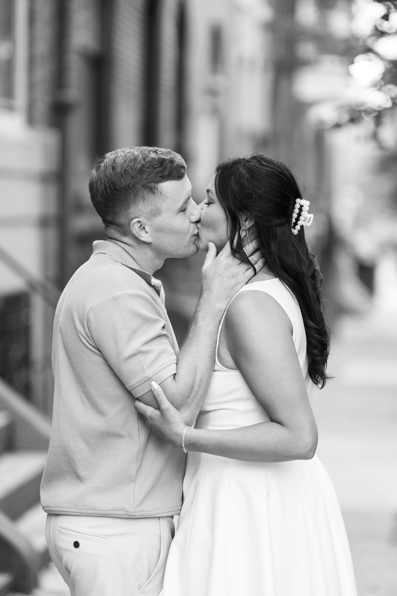A couple shares a tender moment in black and white photography on a city street.