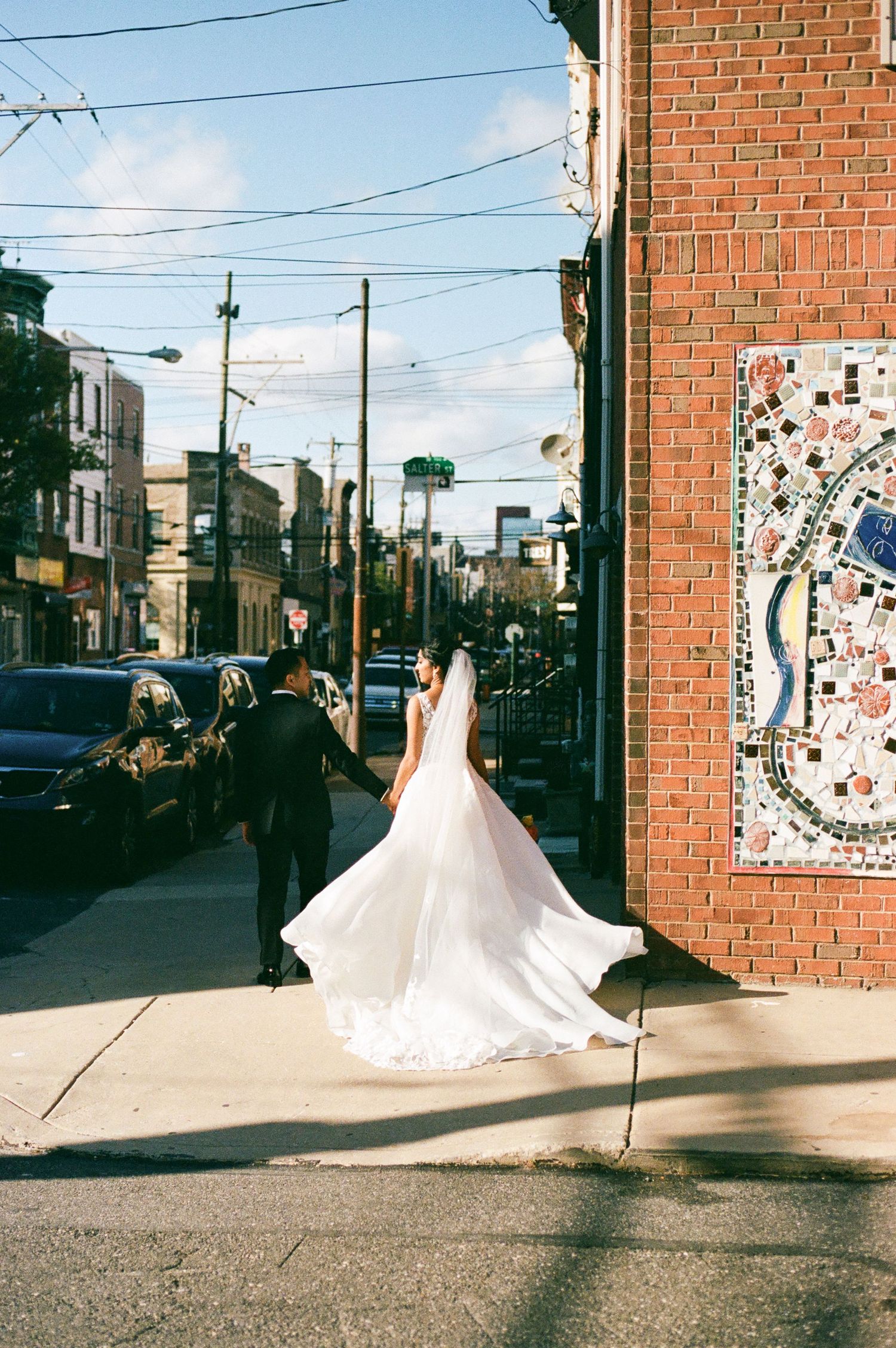 White wedding dress flowing dramatically against urban brick wall backdrop.