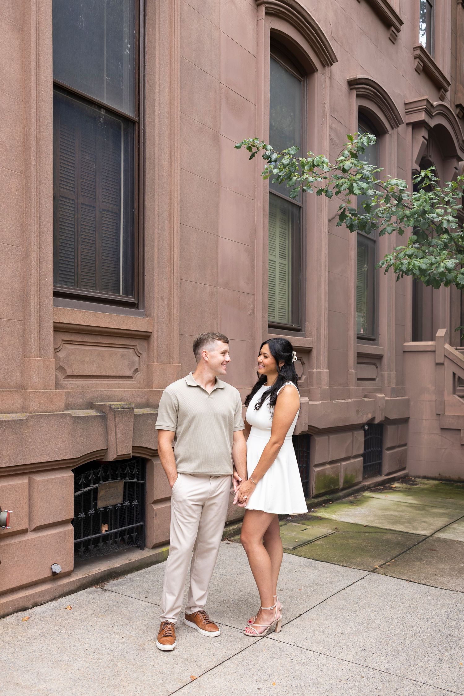 Couple sharing playful moments against brownstone building during engagement session.