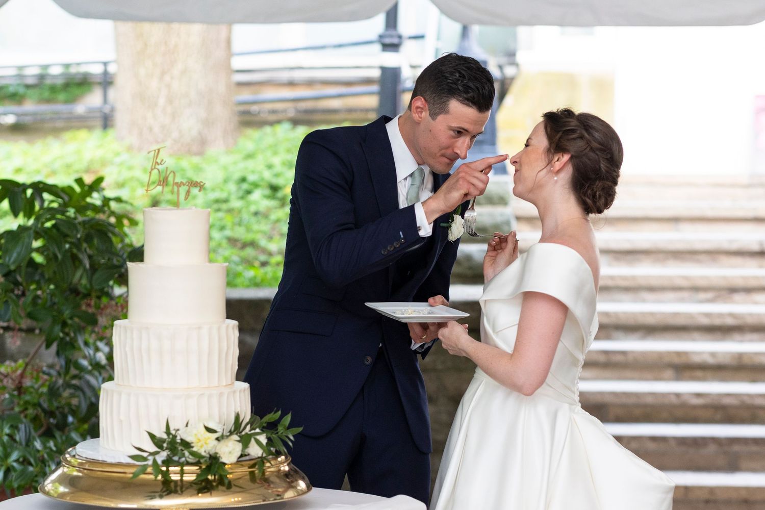 Playful cake feeding moment between newlyweds at their outdoor wedding reception.