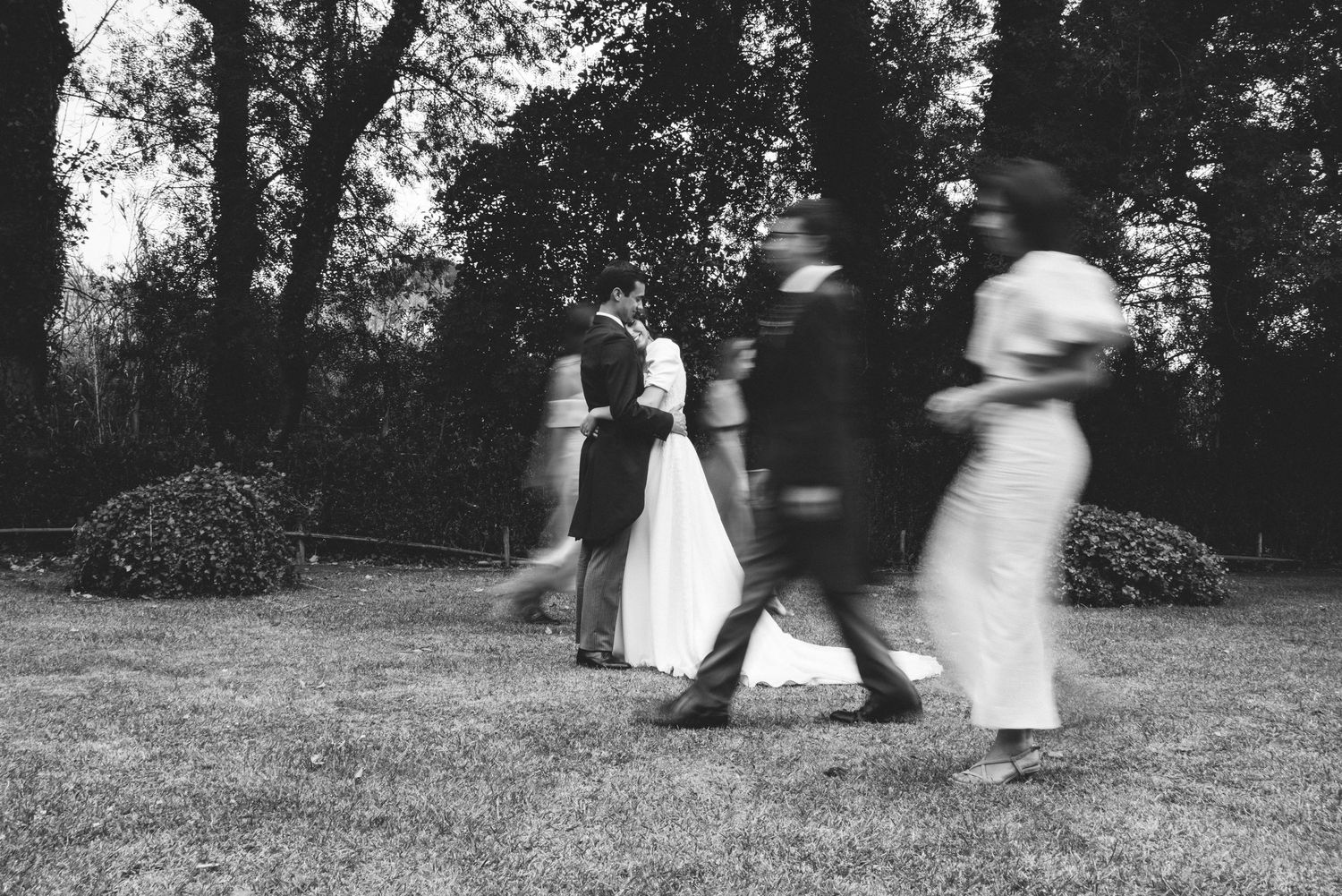 Candid black and white wedding photograph of bride and groom with some guests