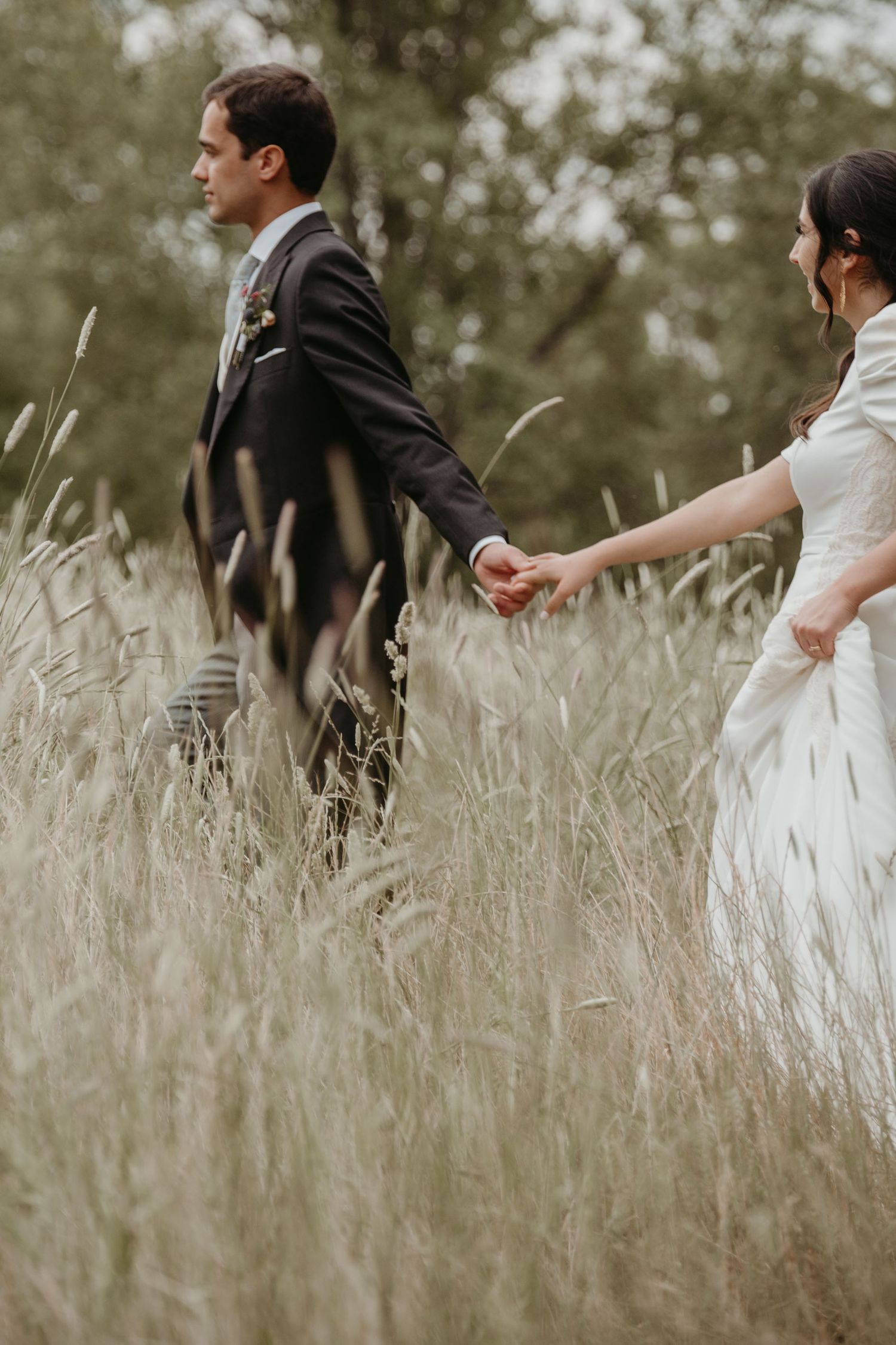 Bride and groom walking hand in hand through tall grass on their wedding day