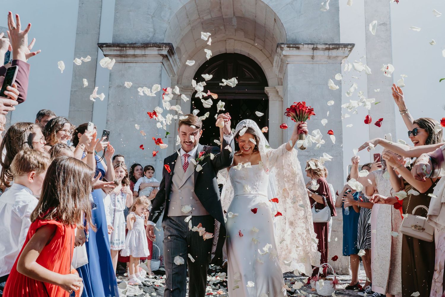 Newlyweds leaving the church surrounded by guests and flower petals