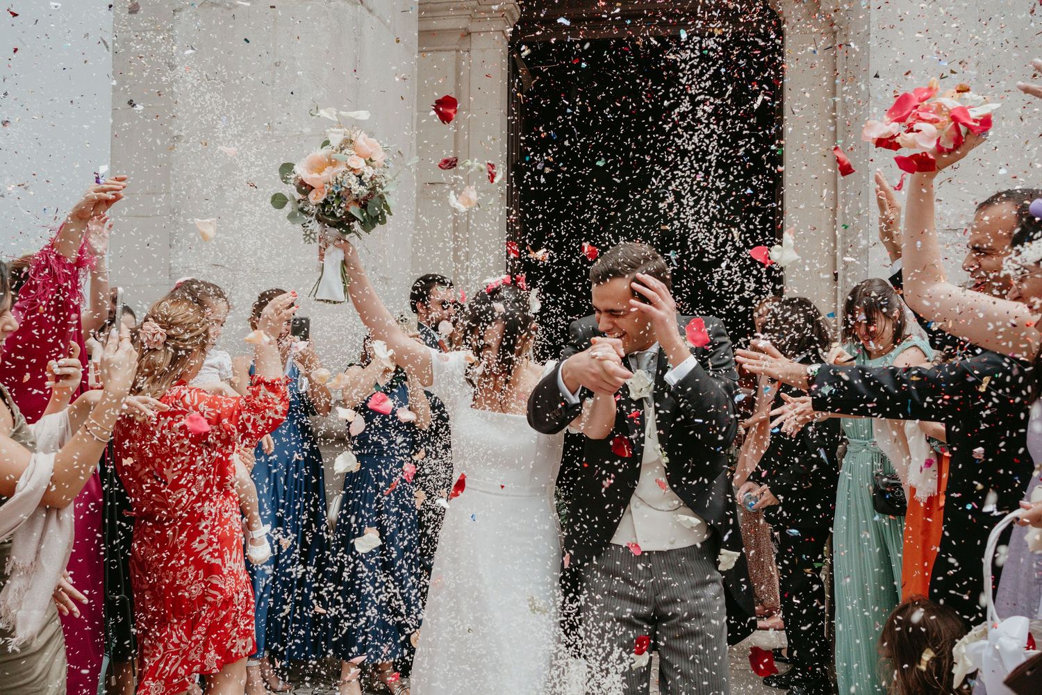 Joyful bride and groom leaving their wedding ceremony surrounded by guests and confetti