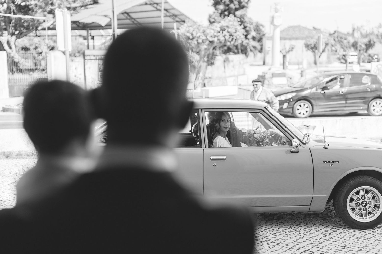 Candid wedding moment with guests watching the bride arriving in a vintage car.