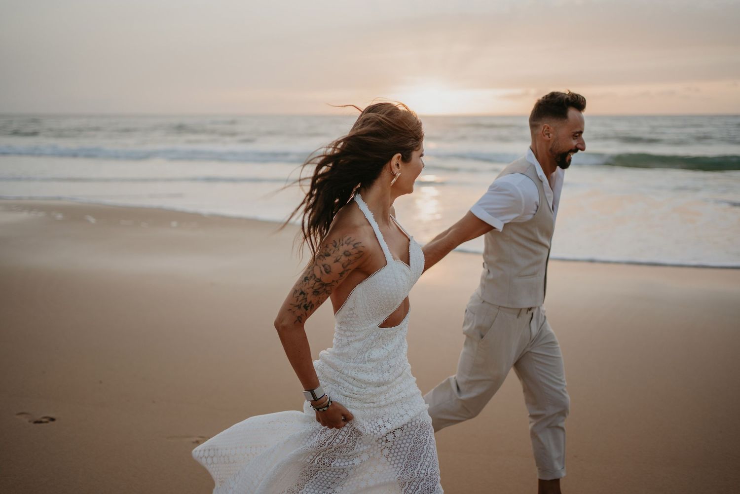 Couple running barefoot along the beach on their wedding day