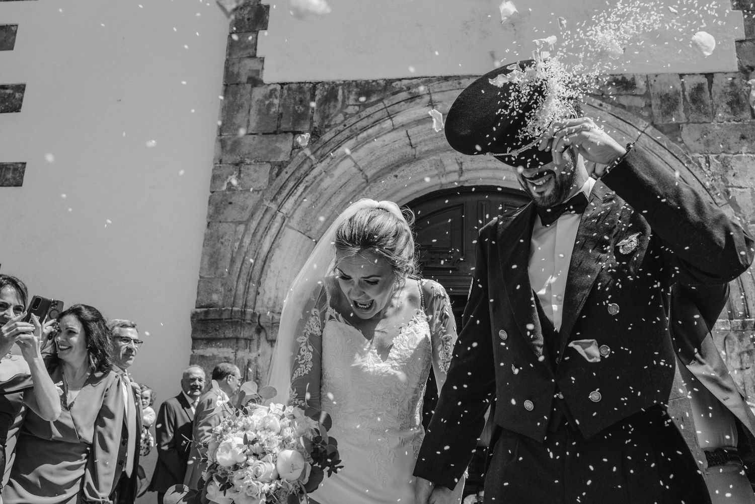 Emotional bride and groom leaving their wedding ceremony surrounded by guests in Portugal