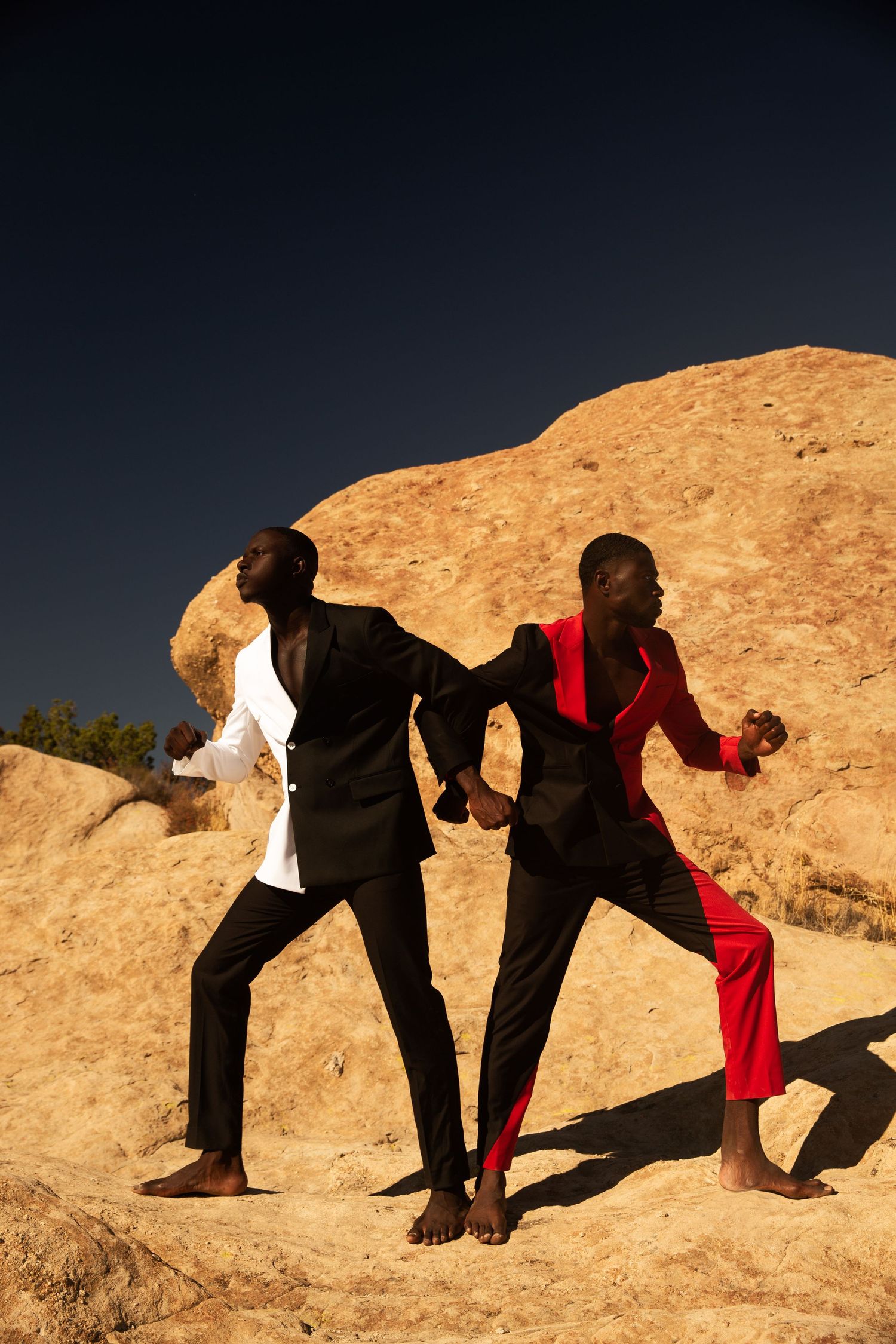 Three people in black and red outfits bend over in a playful pose against a desert landscape at sunset. photo by Tayo Jr. PZ STUDIO VISUALS