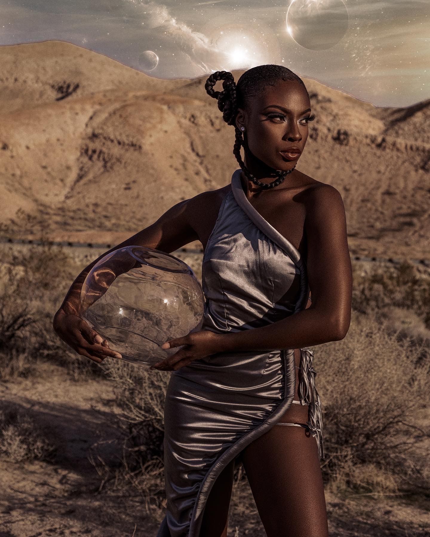 Fashion model in silver dress poses against desert landscape with dramatic sky and planets. PZ STUDIO VISUALS