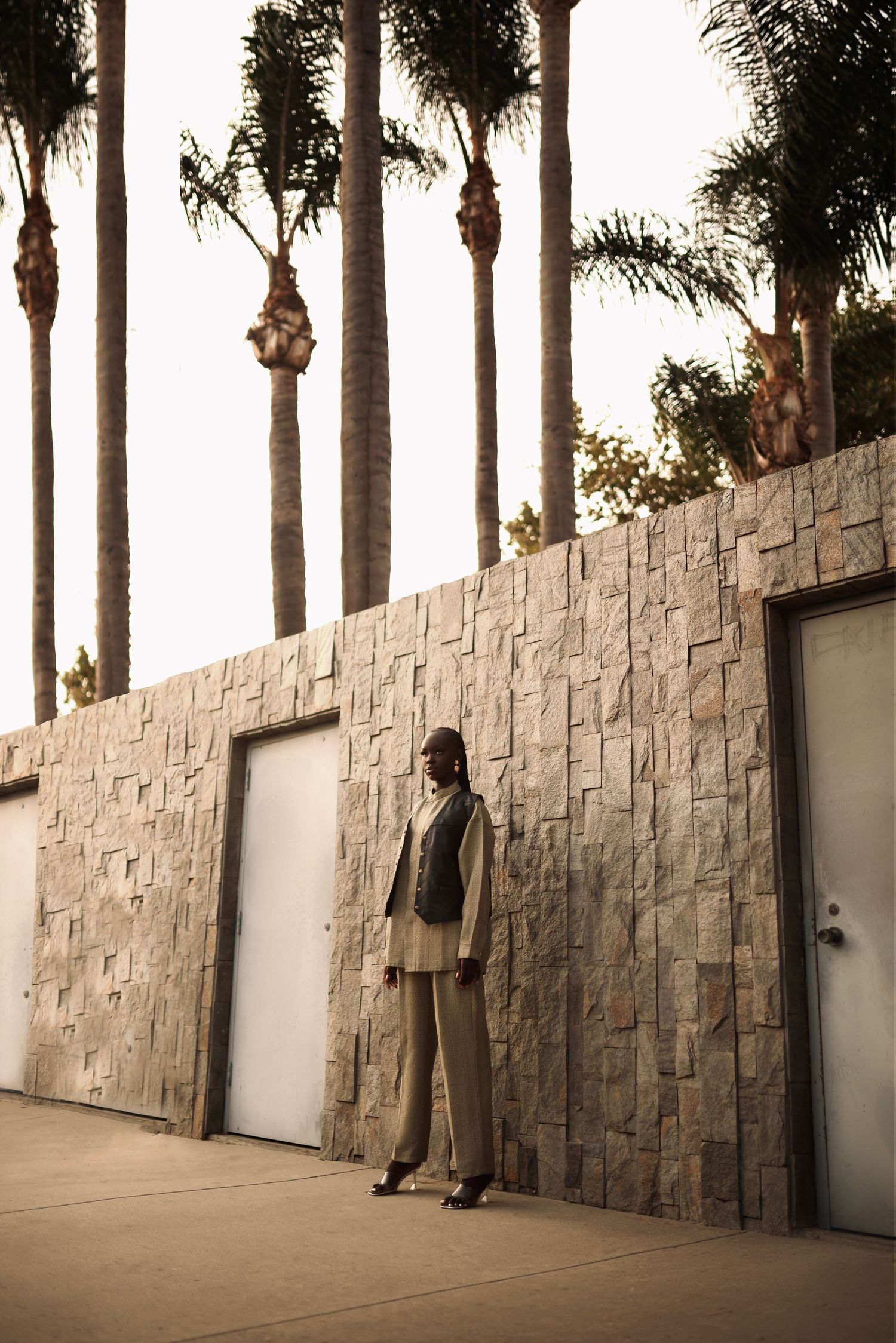 Minimalist fashion portrait against stone wall with palm trees.PZ STUDIO VISUALS
