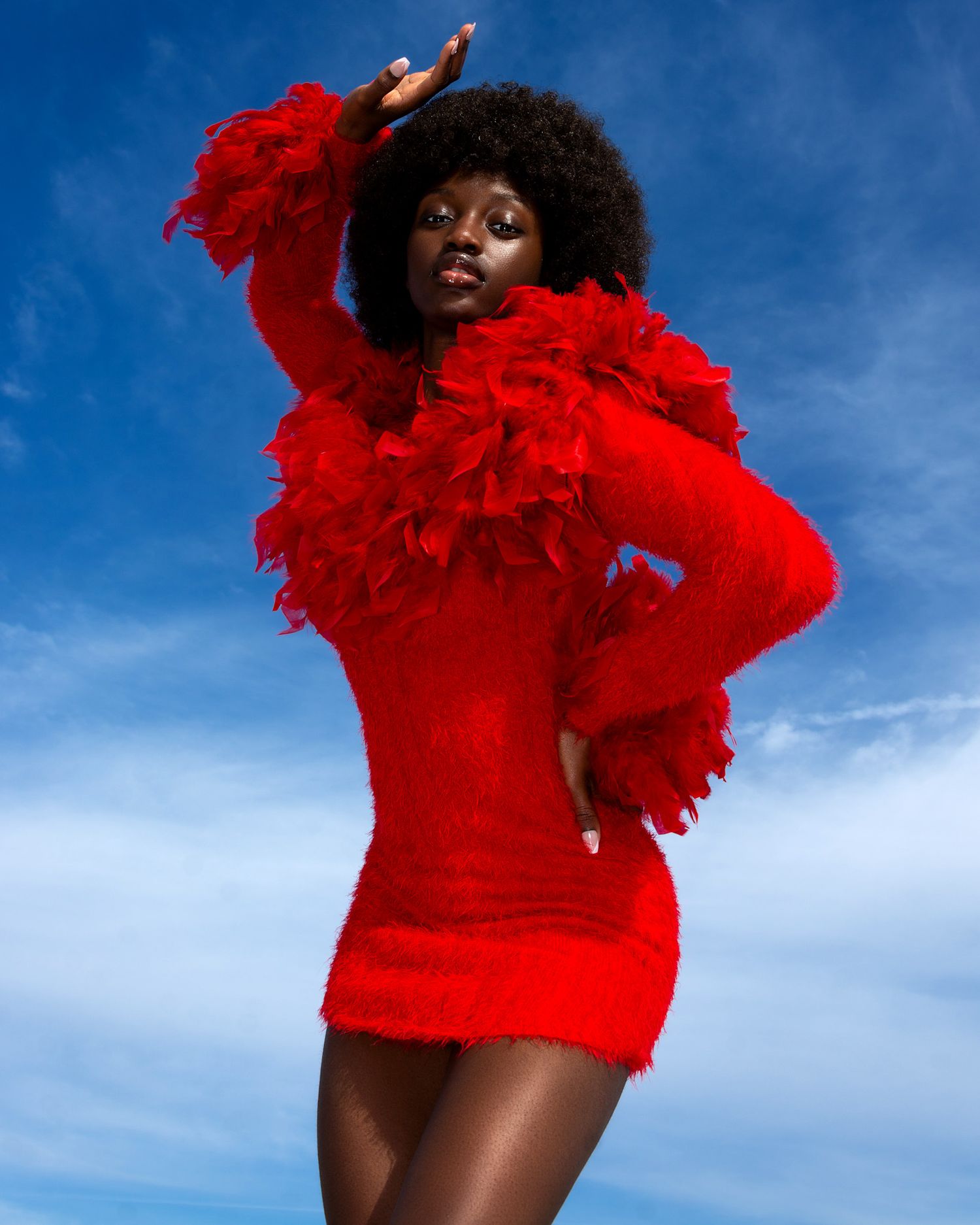 Dynamic fashion shots of model in bright red feathered outfit against blue sky. PZ STUDIO VISUALS