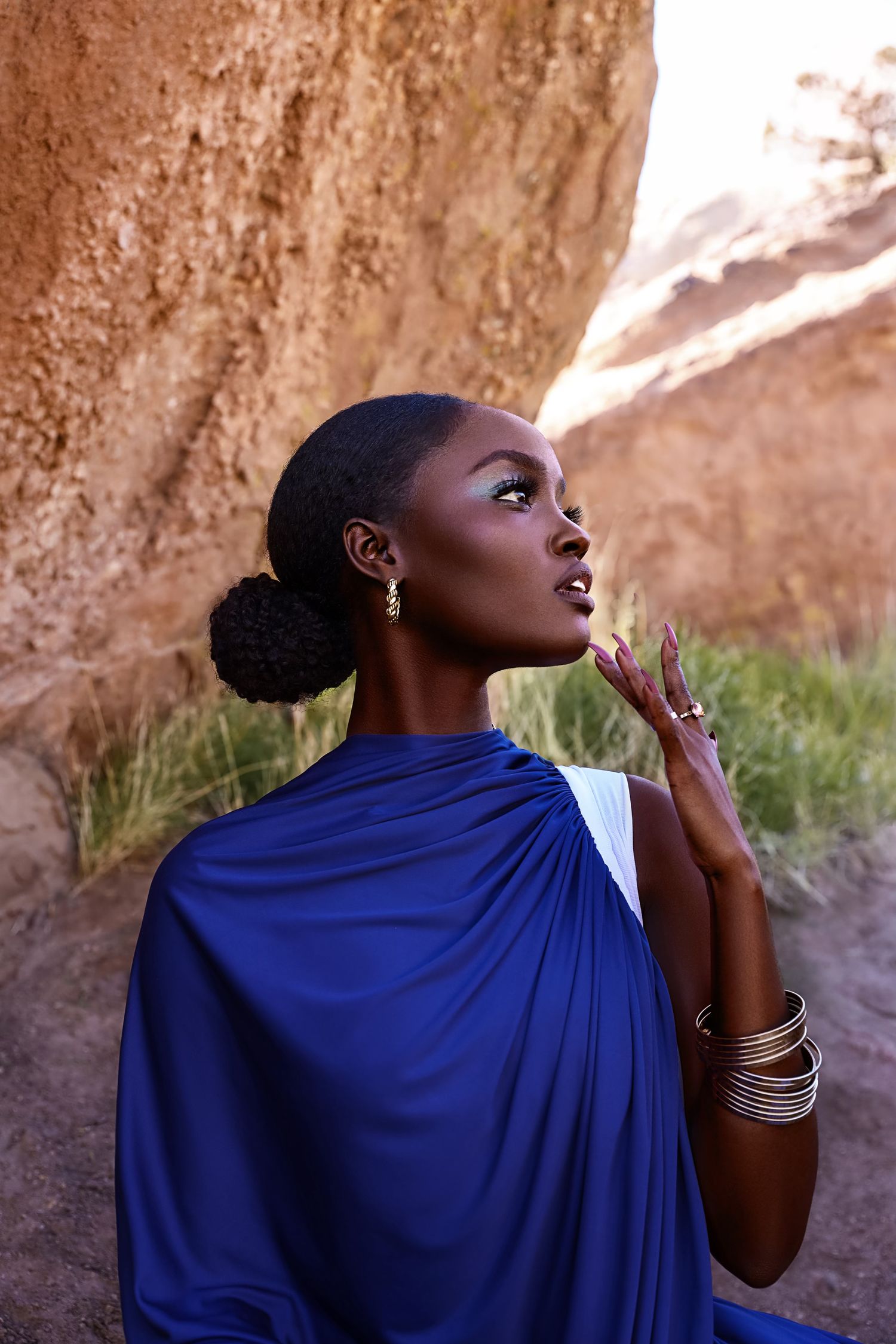 Elegant portrait in flowing blue draped garment against desert rock formation. PZ STUDIO VISUALS
