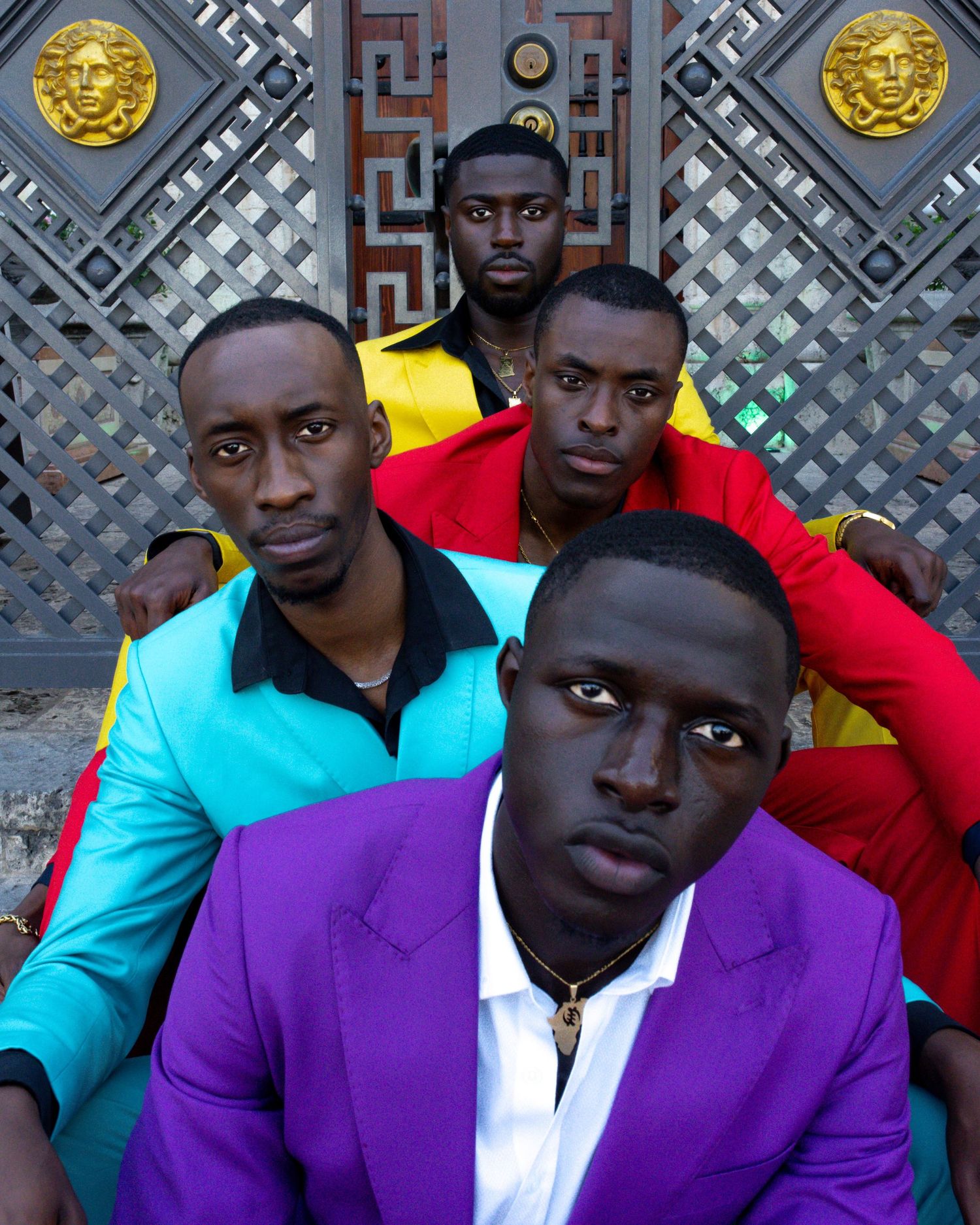 Group wearing vibrant purple and turquoise suits posing against a decorative metallic backdrop.PZ STUDIO VISUALS