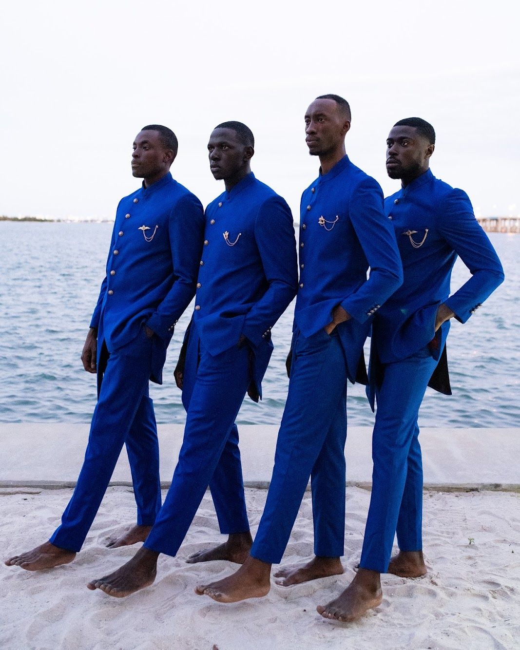 Four people in matching blue outfits sit in a row on a sandy beach near the ocean. PZ STUDIO VISUALS
