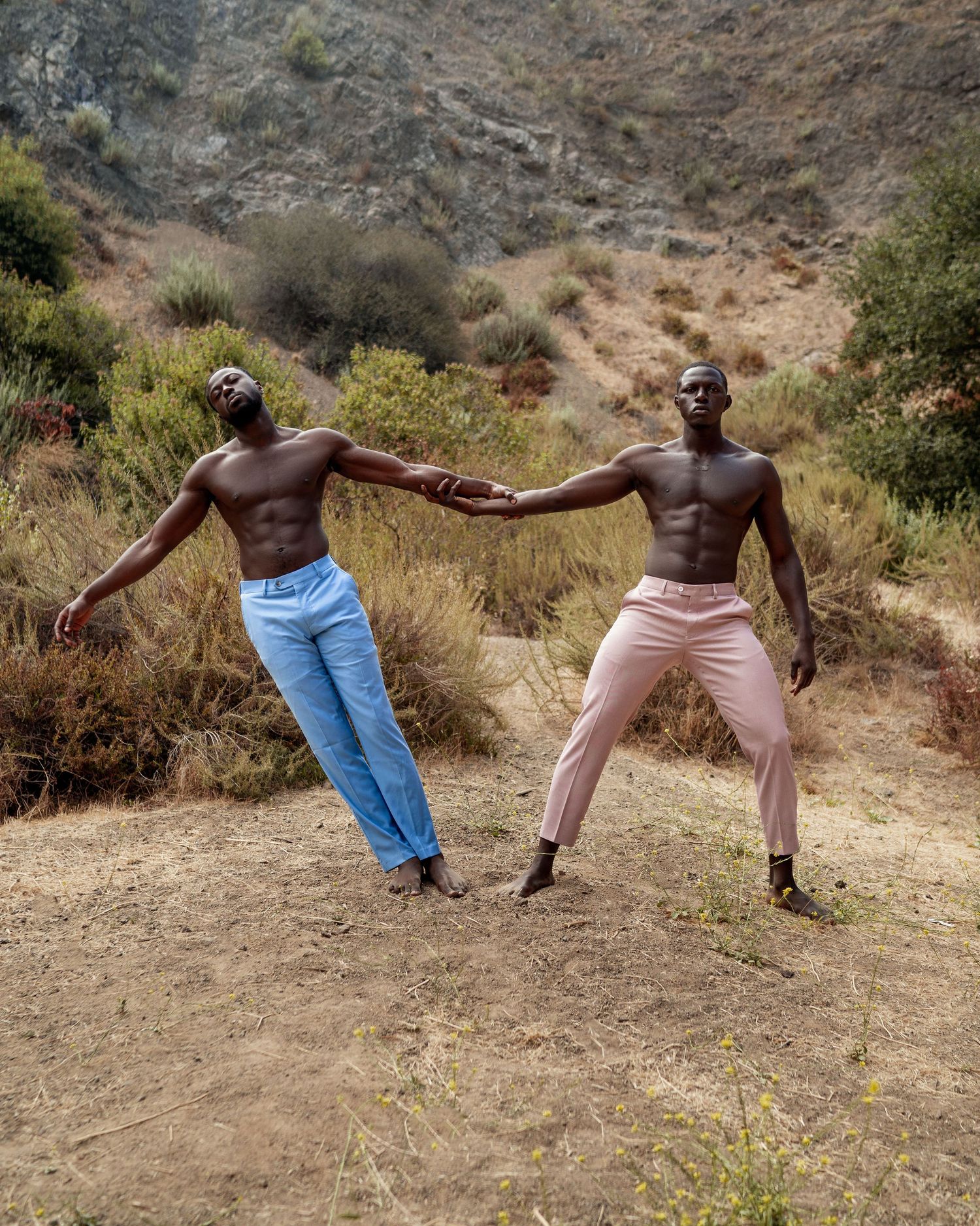 Two people perform a synchronized pose move on a dirt path against a hillside backdrop. PZ STUDIO VISUALS