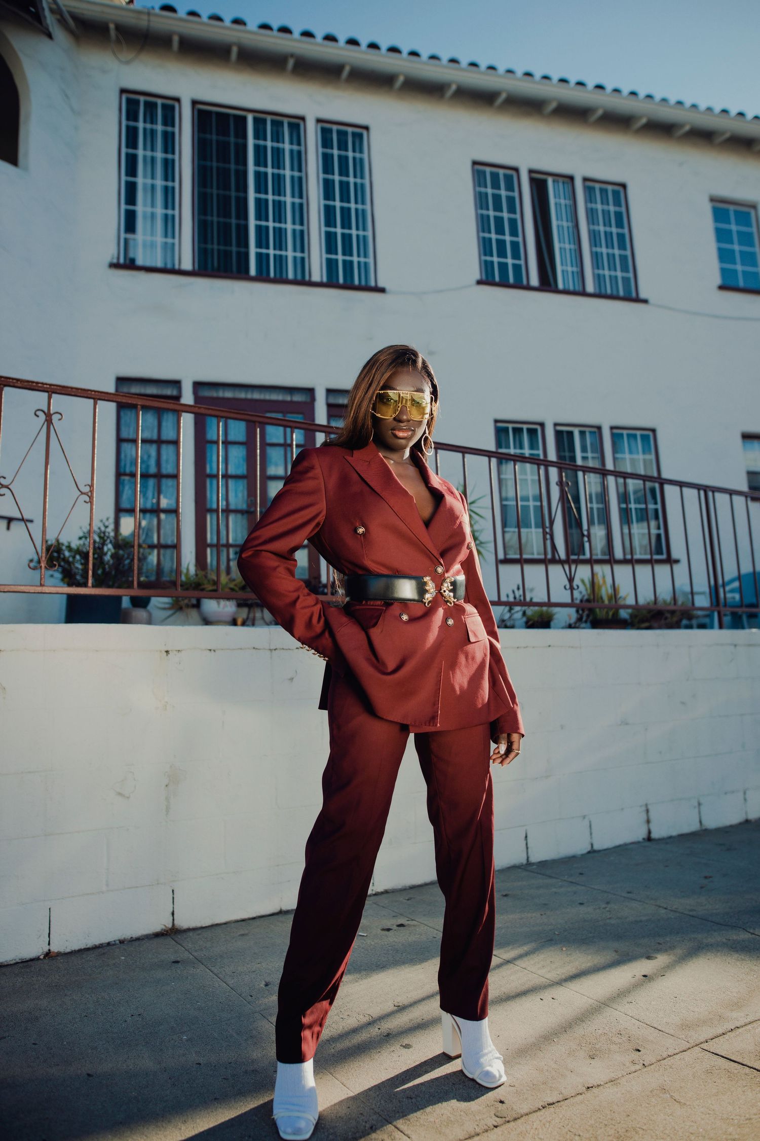 Street style fashion in burgundy suit and white sneakers against Spanish-style architecture. PZ STUDIO VISUALS
