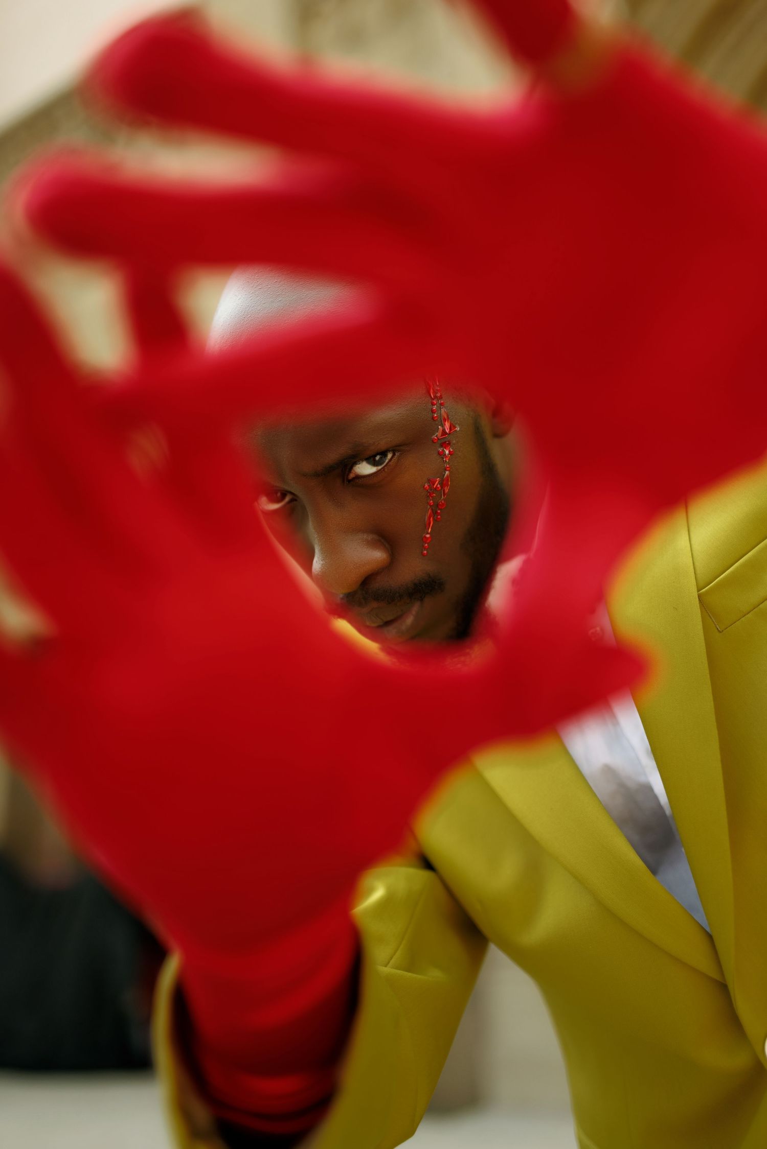 Artistic portrait through red foreground element wearing yellow jacket with decorative face details. PZ STUDIO VISUALS