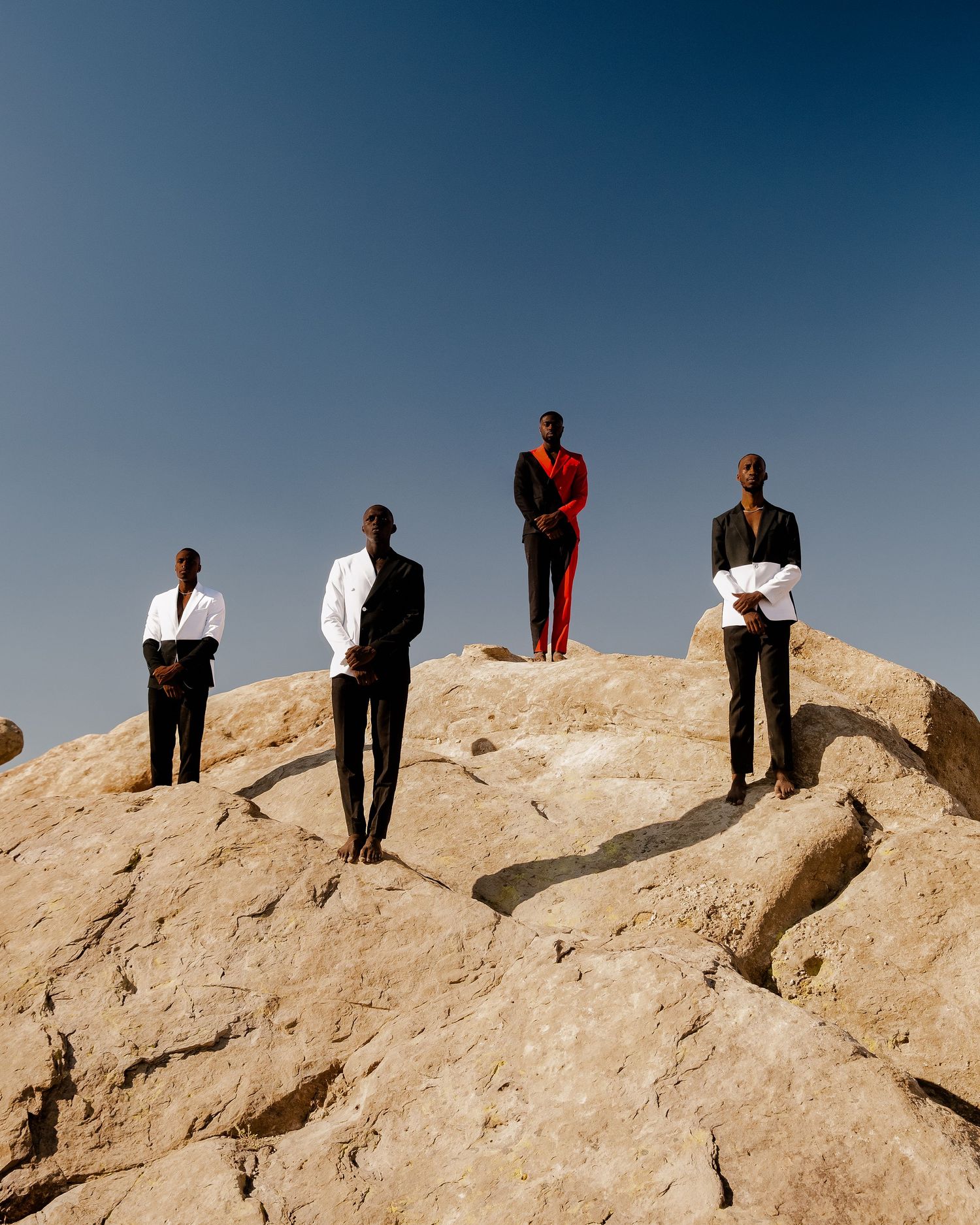 People stand silhouetted against a blue sky on top of a rocky desert ridge formation. by Tayo jr produced and styled by PZ STUDIO VISUALS