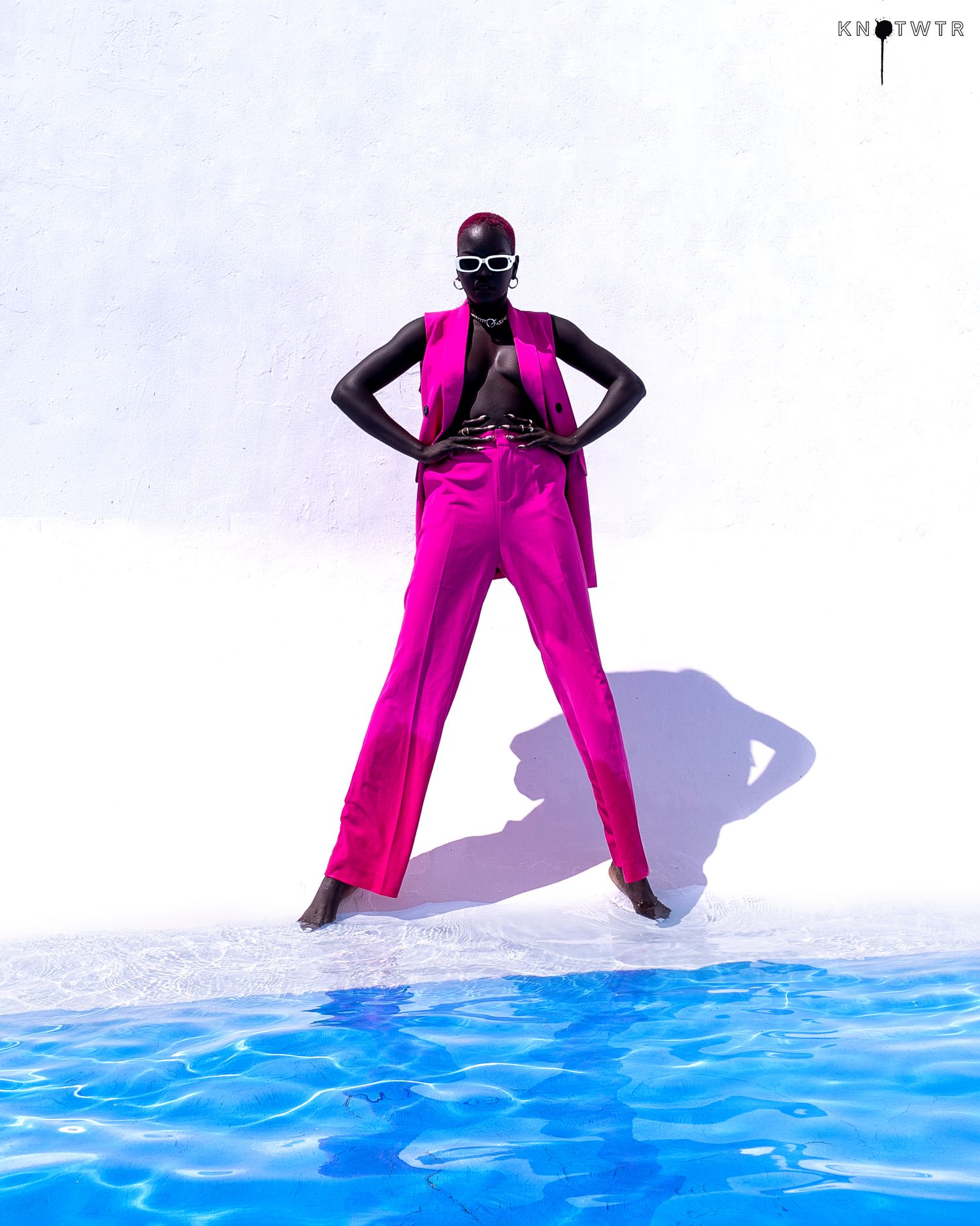 Figure in hot pink attire poses dramatically against a blue water background. Nyamkim styling by PZ STUDIO VISUALS