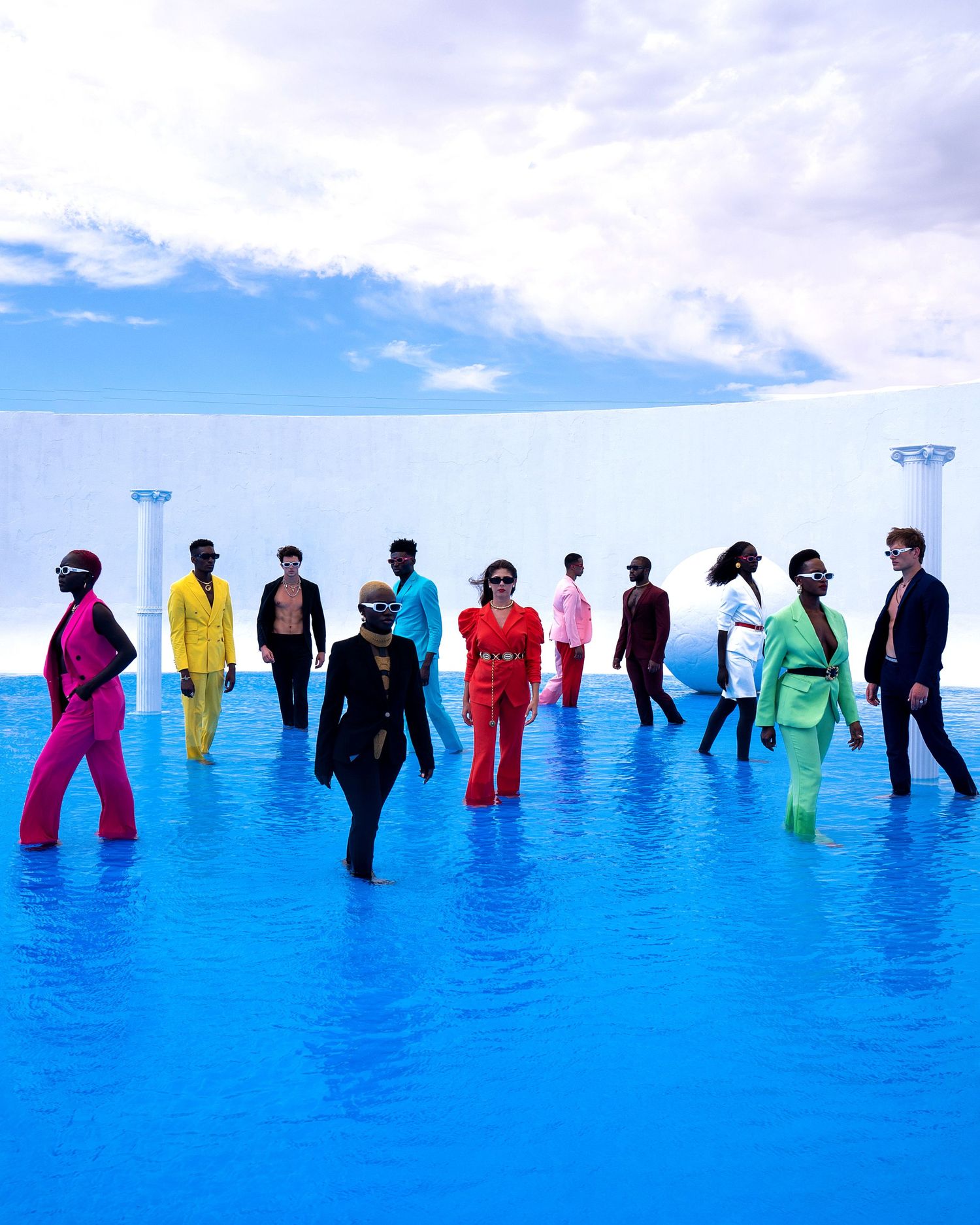 People in colorful outfits stand in bright blue water creating a striking visual contrast against the cloudy sky. PZ STUDIO VISUALS