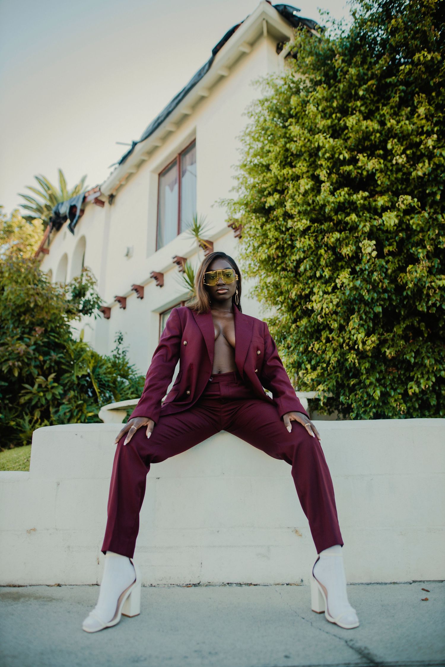 Bold pose in burgundy suit and white boots against residential backdrop. PZ STUDIO VISUALS