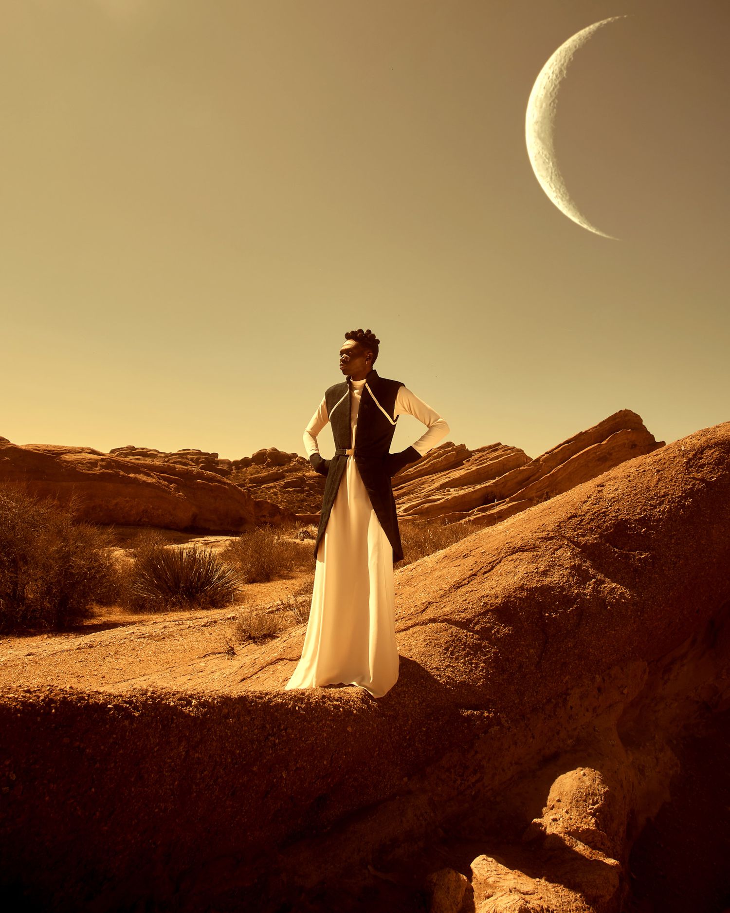 Silhouette stands on desert rocks during sunset with crescent moon in sepia-toned scene. Isaak Adoyi PZ STUDIO VISUALS