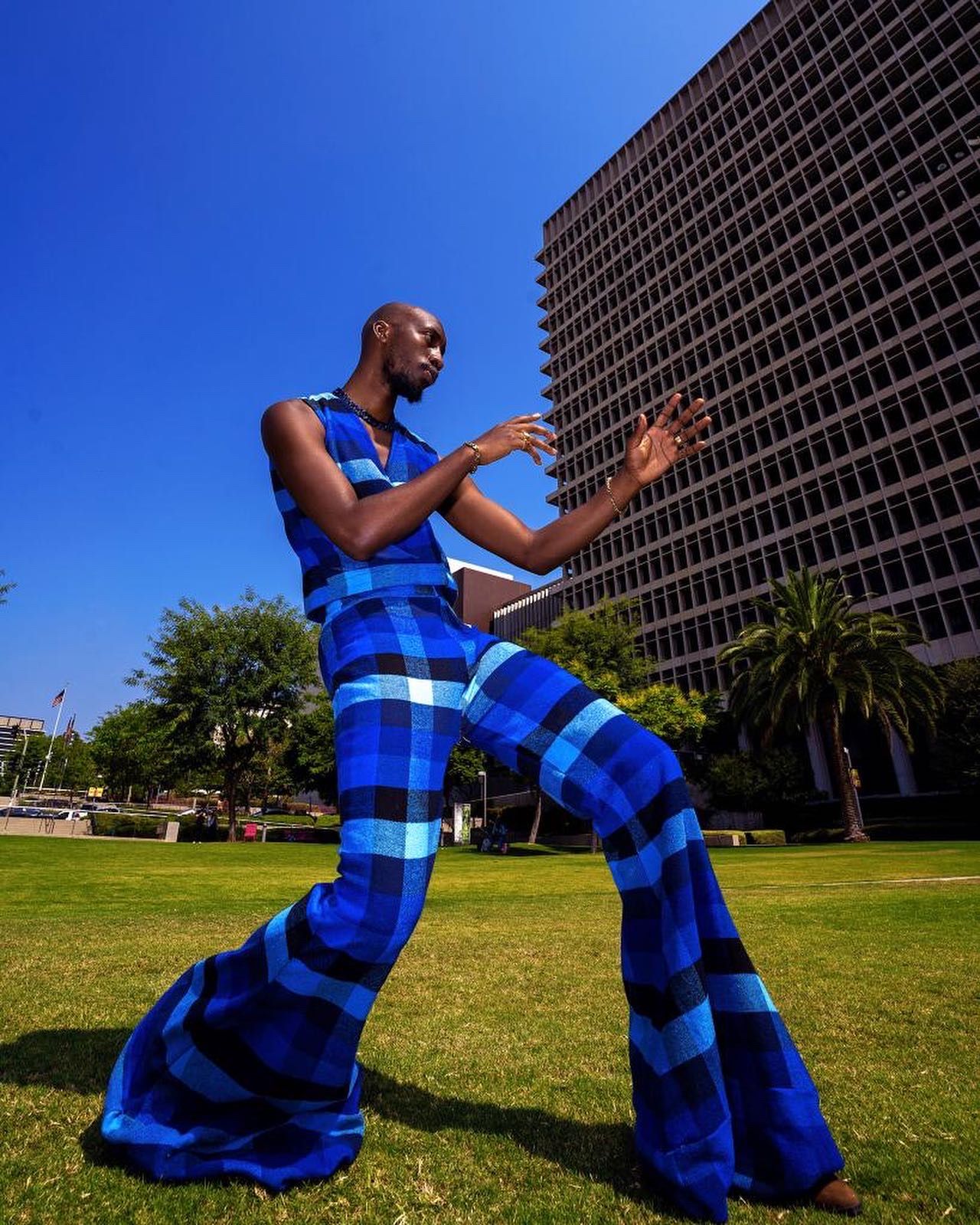 Dramatic pose in blue checkered flared pants against urban skyline. PZ STUDIO VISUALS Kalema Jon