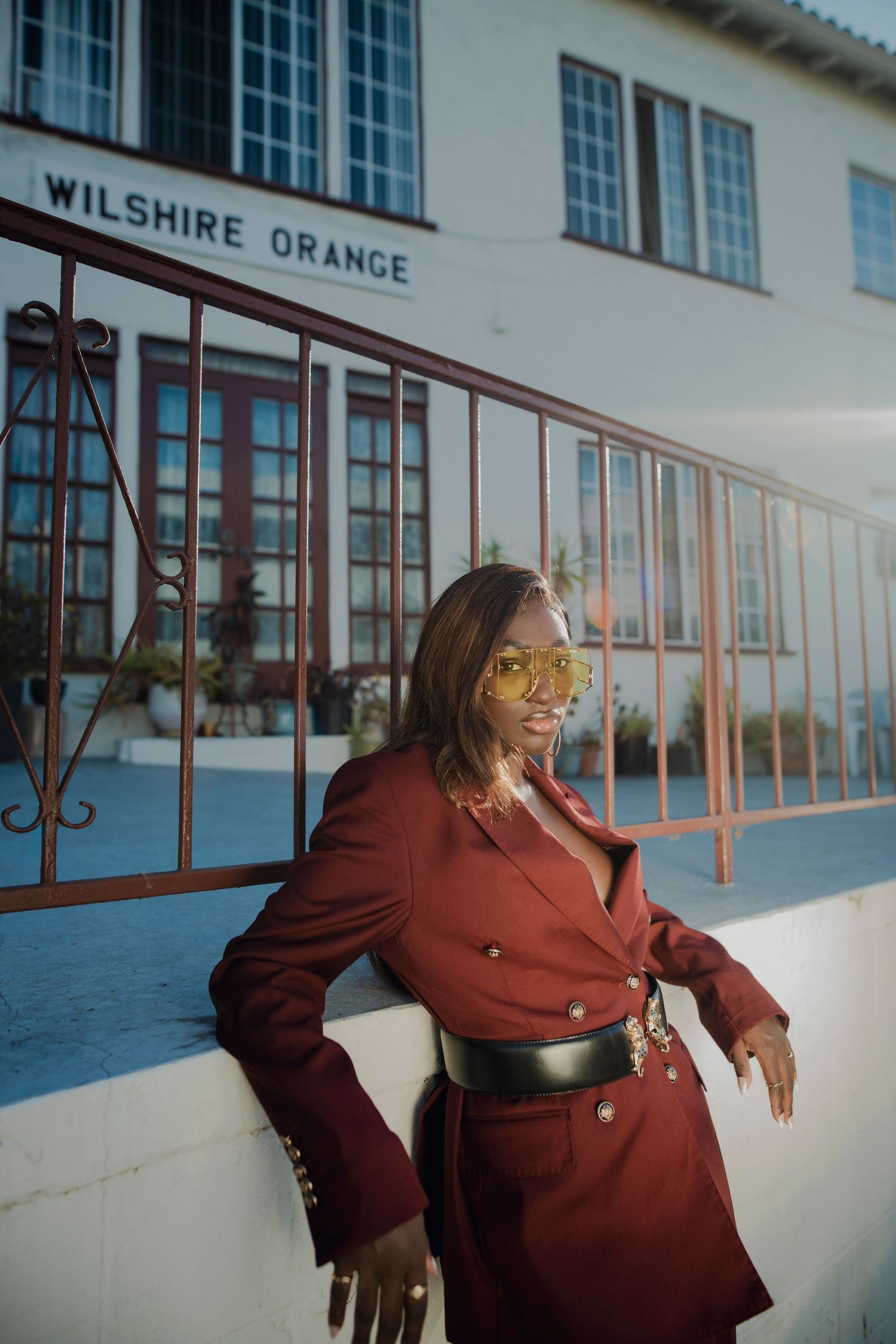 Fashion editorial with model in brown coat posing against white building exterior. PZ STUDIO VISUALS