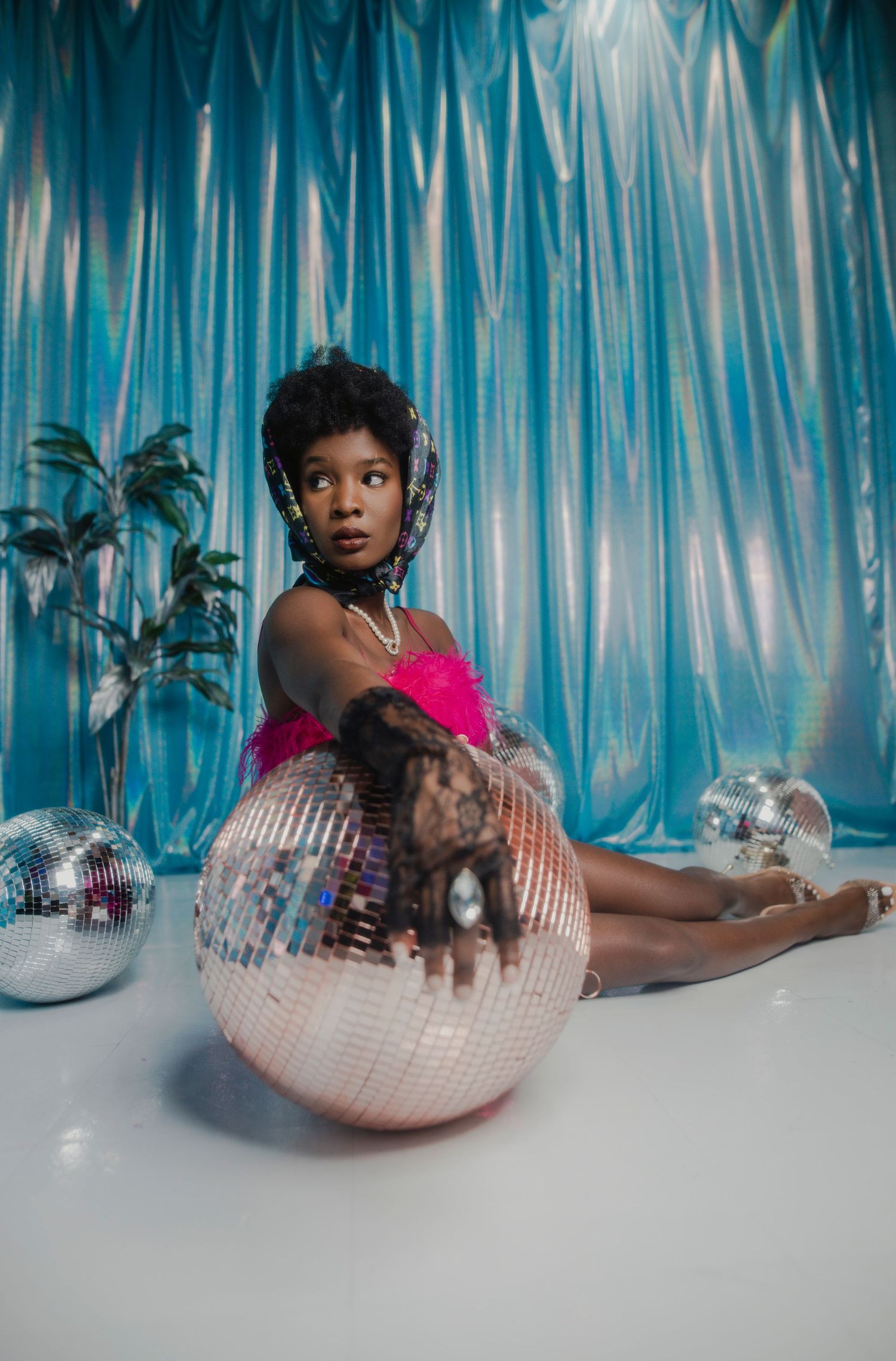 A figure in pink poses with disco balls against a blue draped backdrop in a dreamy studio setting. PZ STUDIO VISUALS