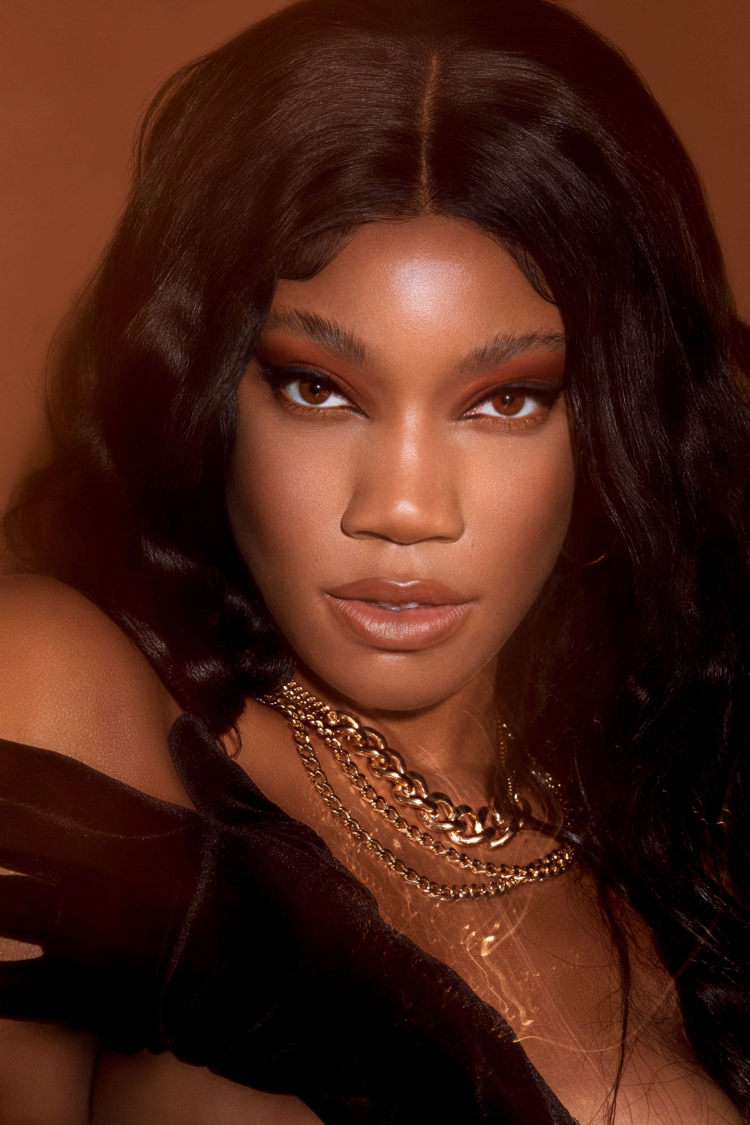 Fashion portrait with dramatic lighting featuring gold chain necklaces against a warm brown background. PZ STUDIO VISUALS