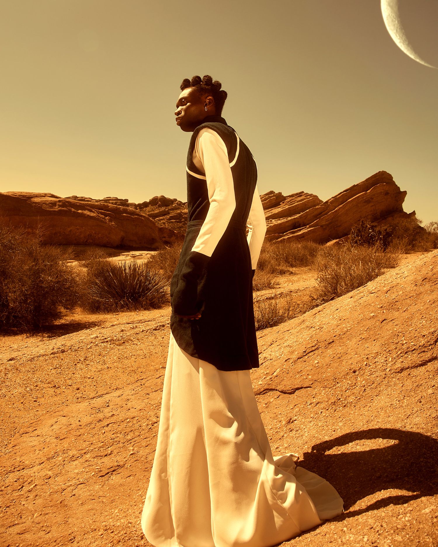 Fashion portrait in desert setting with flowing white dress and black vest against golden sunset sky. Isaak Adoyi for PZ STUDIO VISUALS