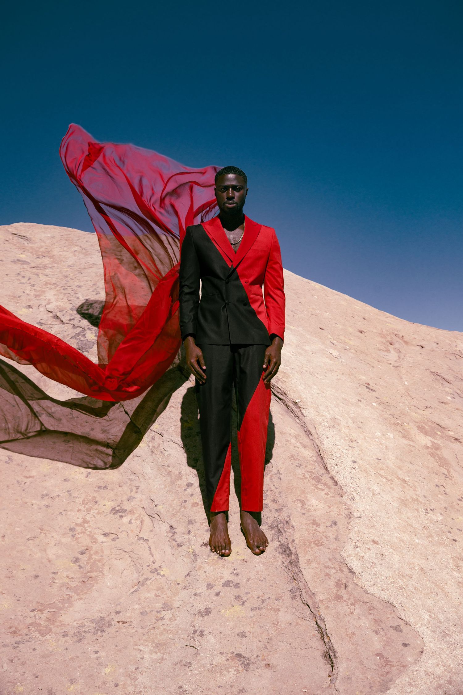 A figure in black clothing with flowing red fabric stands dramatically against a white rocky landscape. PZ STUDIO VISUALS