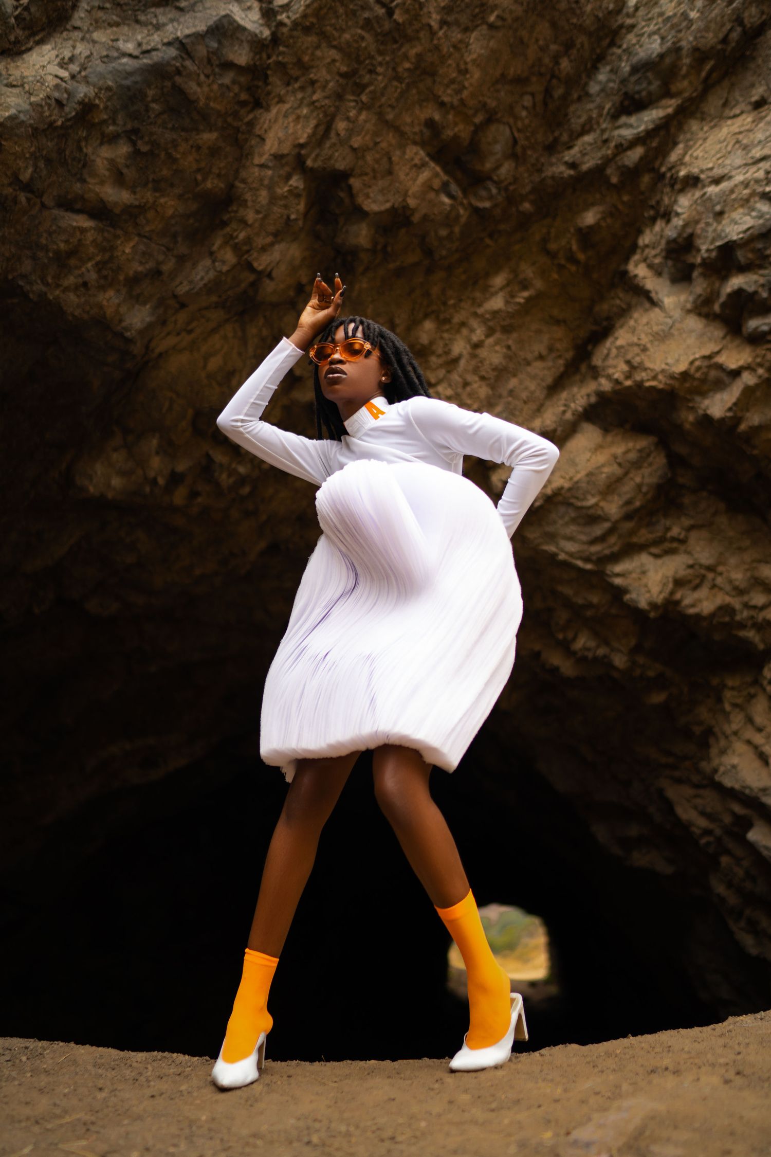 A dancer in a white dress and yellow boots performs dynamic movements against a rocky cave backdrop. PZ STUDIO VISUALS