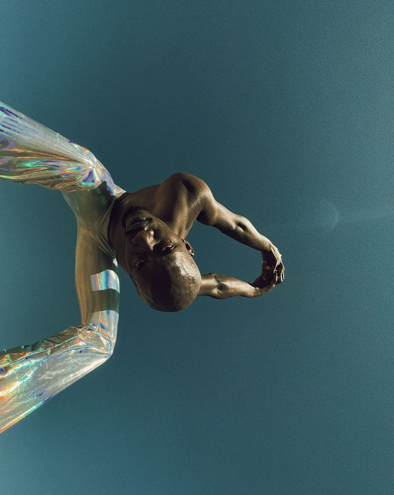 Underwater dancer in flowing iridescent fabric creates graceful movement against turquoise background.