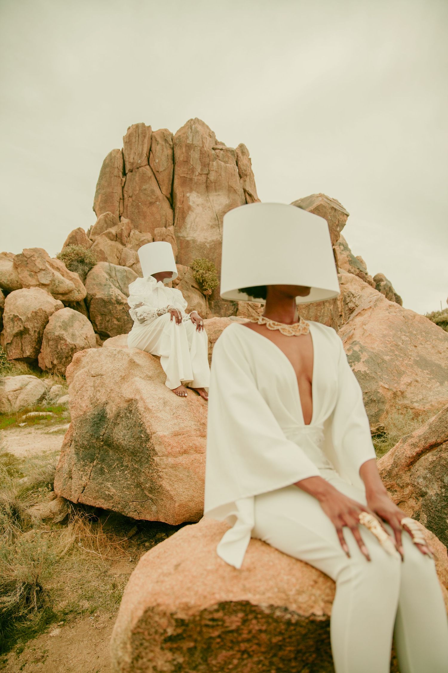 Person in flowing white garments seated on desert rocks under cloudy sky. PZ STUDIO VISUALS