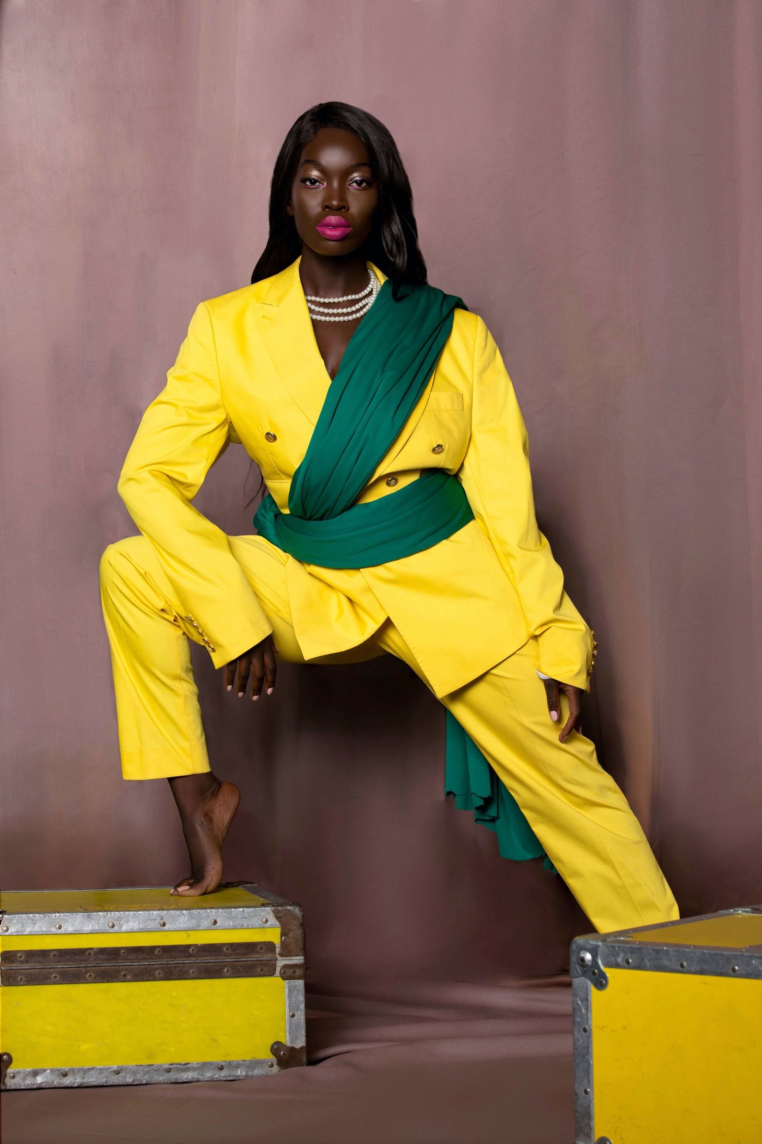 A fashion model in a vibrant yellow suit and emerald green scarf poses elegantly against a brown backdrop. Dora. PZ STUDIO VISUALS