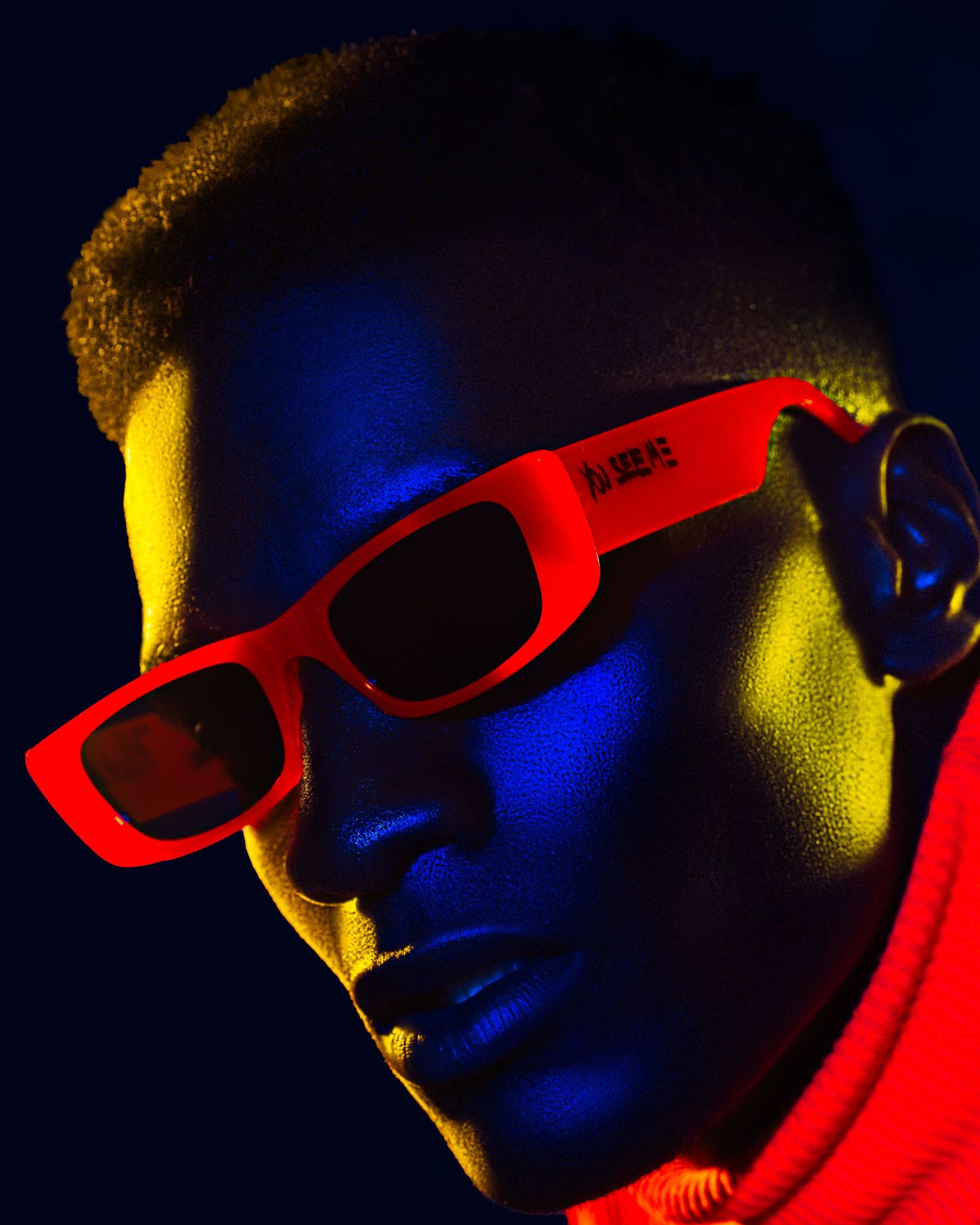 Neon-lit portrait with red sunglasses against dark blue background. PZ STUDIO VISUALS