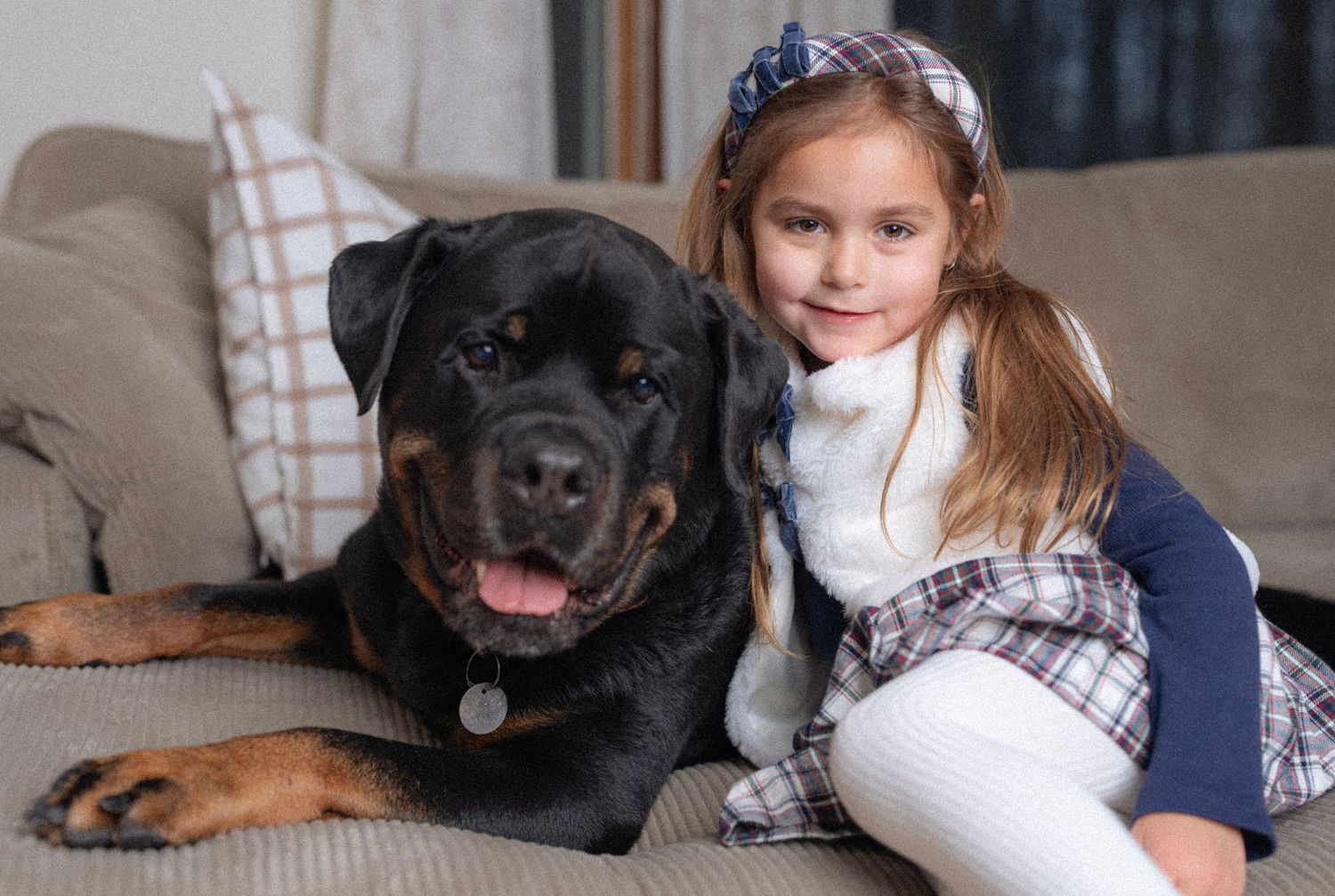 A black Rottweiler relaxes on a light colored couch with children in casual dress.