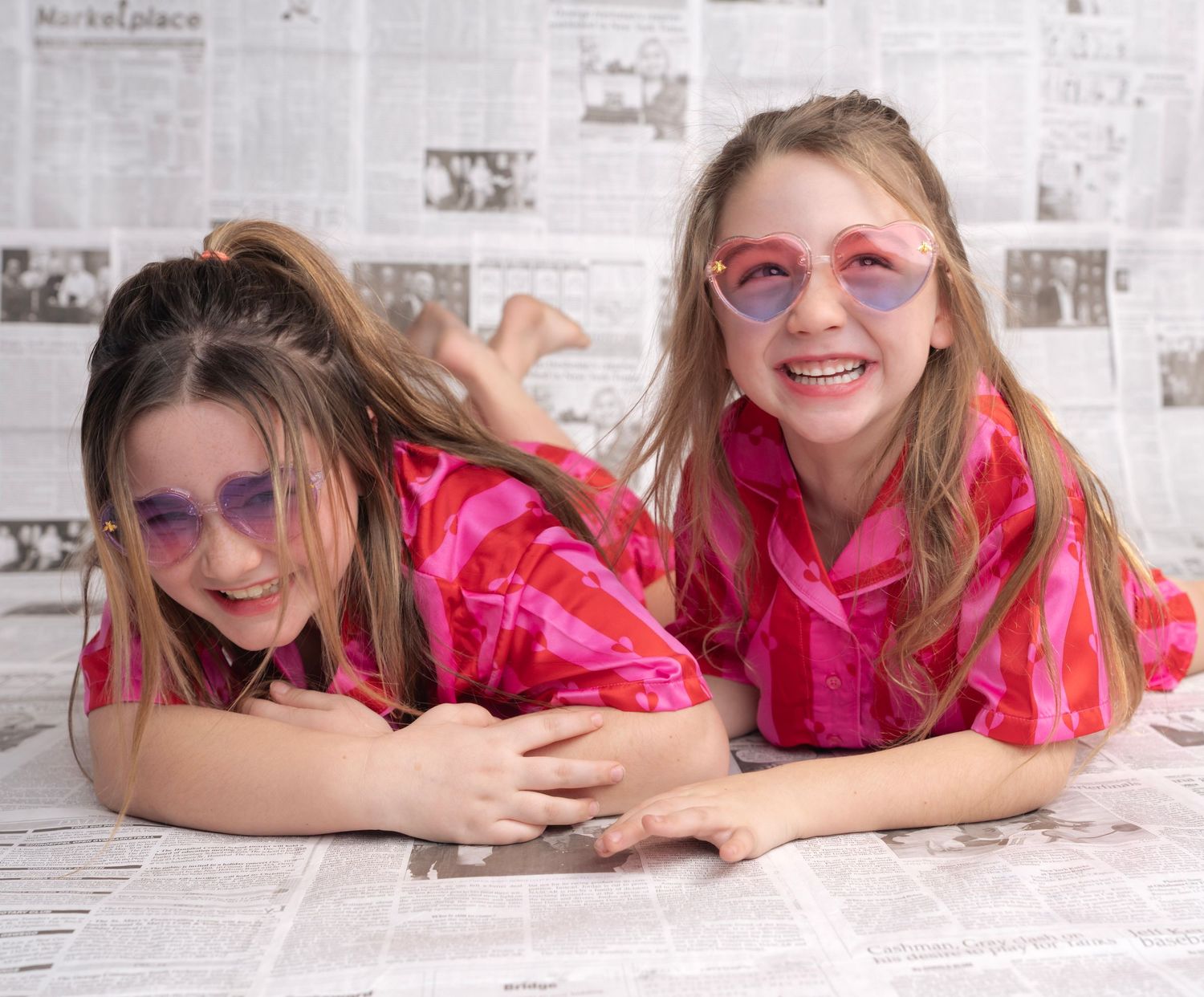 Series of poses lying on newspaper print wearing red and pink outfits.