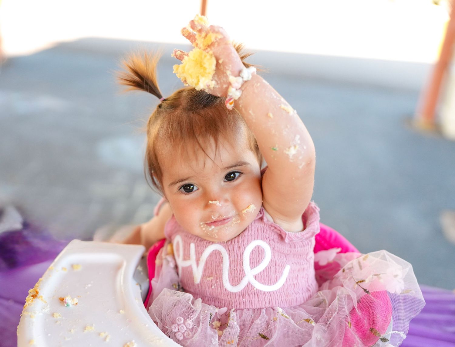 Child in pink dress enjoying messy cake smash celebration.