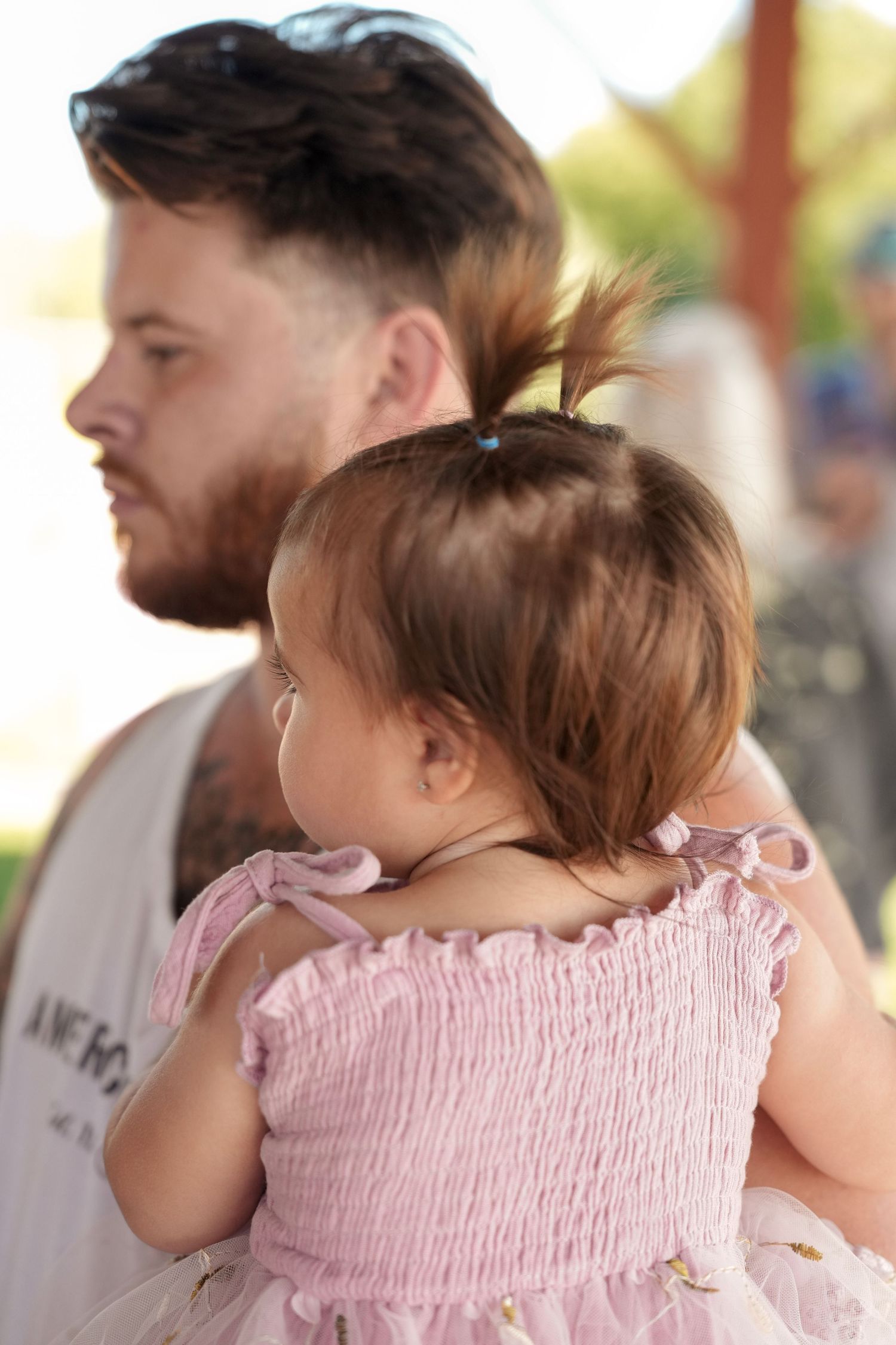 Child being held while wearing pink smocked dress outdoors.
