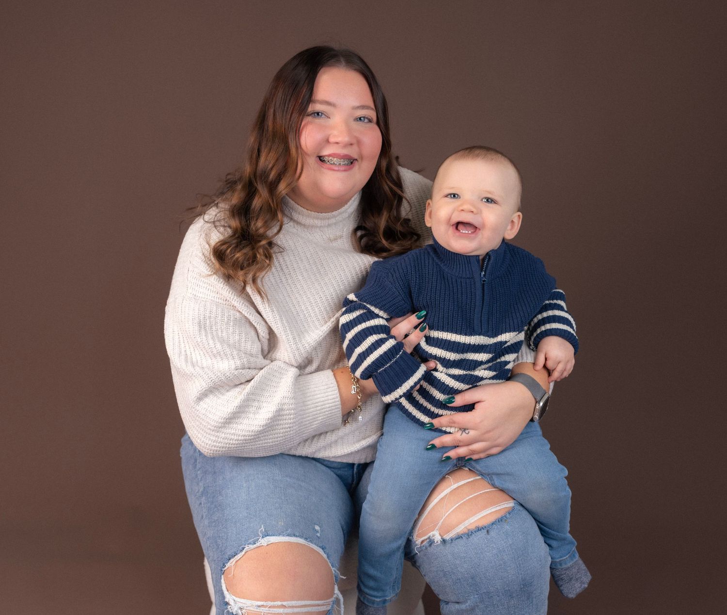 Cozy family moments captured against brown backdrop wearing casual sweaters and jeans.