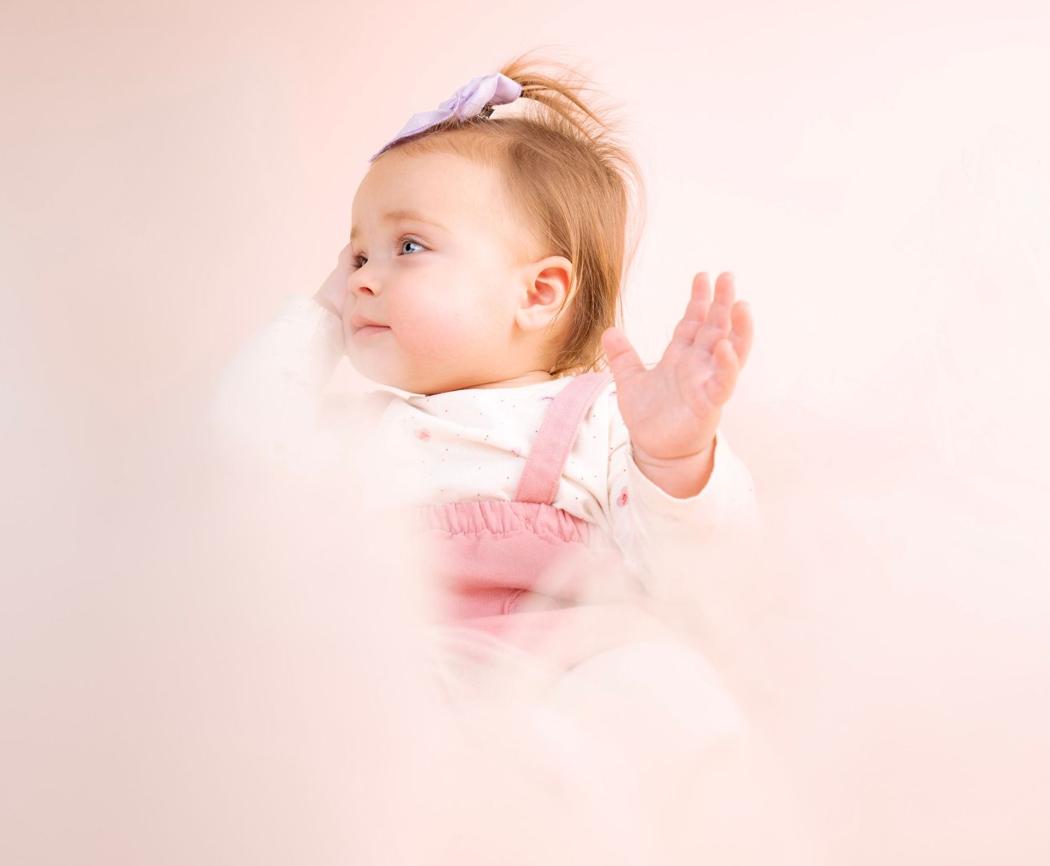 Child in pink dress gazes upward against ethereal pink backdrop.