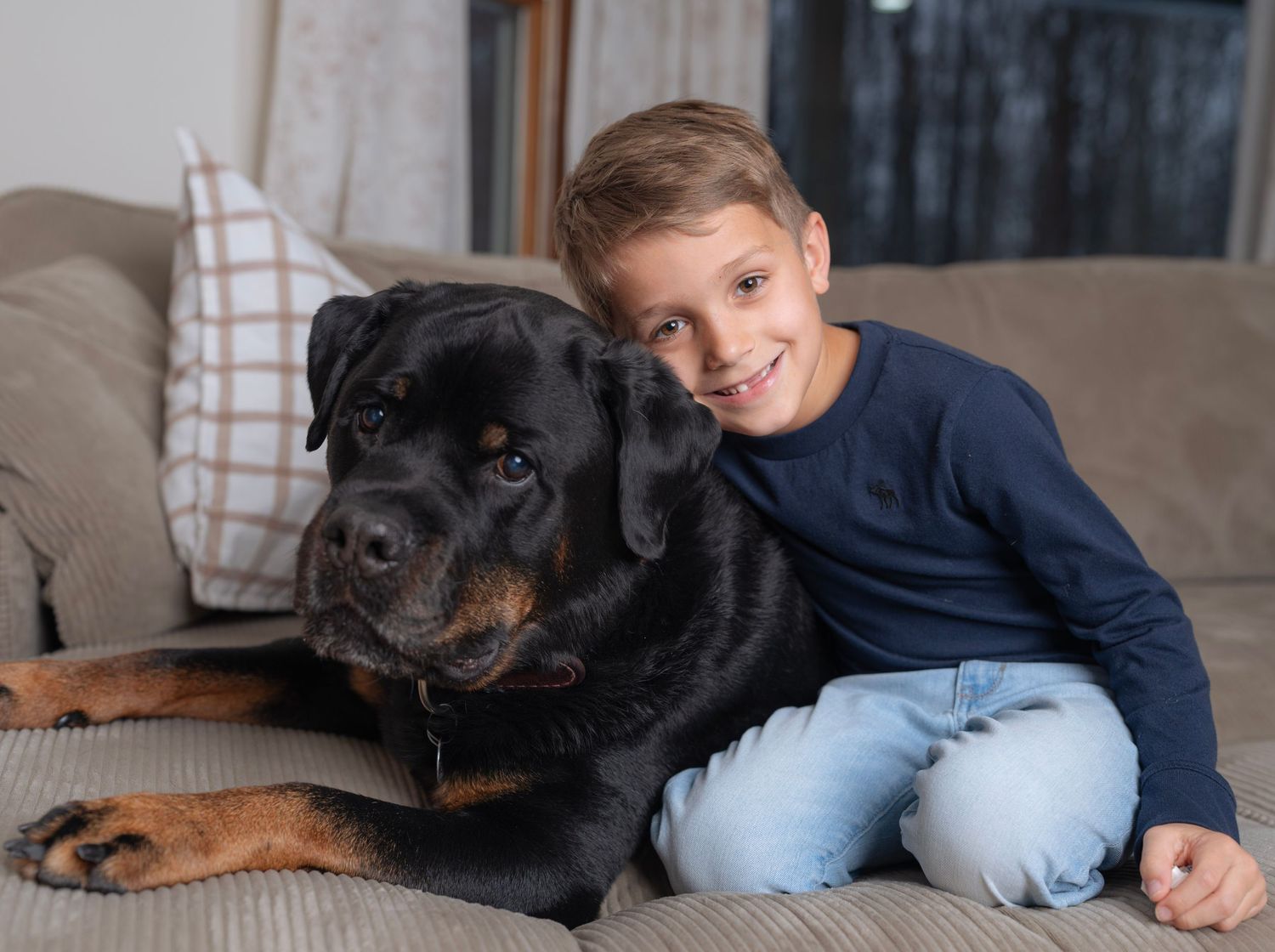 A black Rottweiler dog lounges on a couch with children in casual attire.